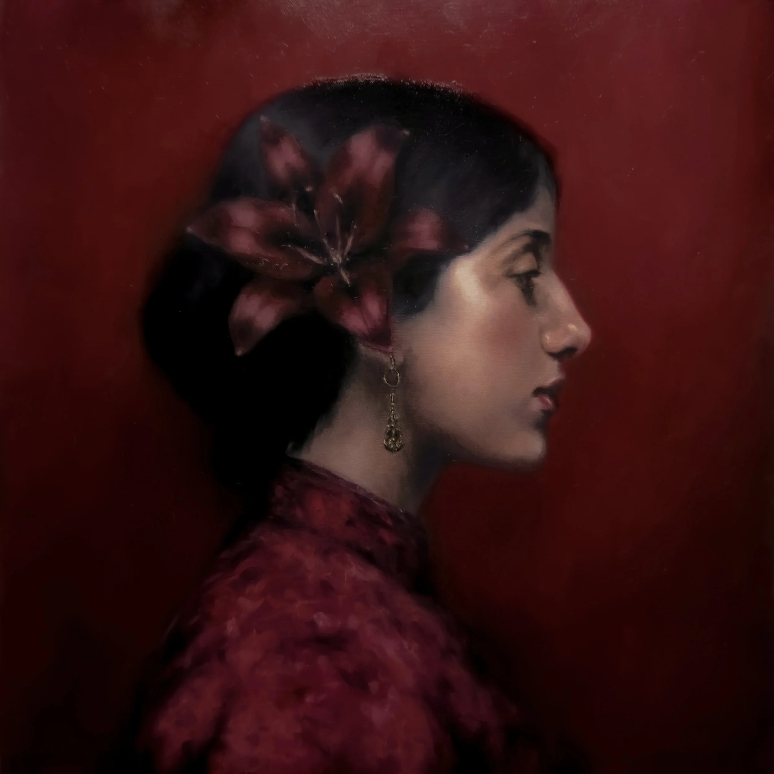 Close-up of a person's face with dark hair and earrings, viewed in profile against a red background.