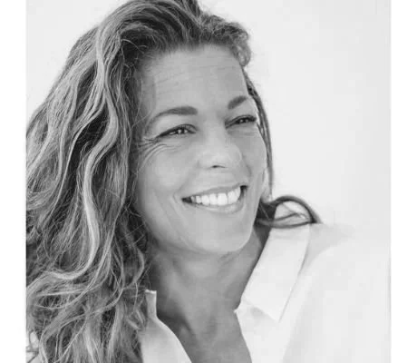 Black and white photo of a smiling woman with wavy hair, wearing a white top.