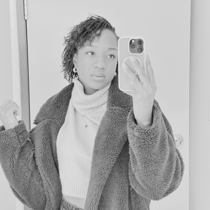 Young woman taking a selfie in a mirror, wearing a fuzzy coat and turtleneck sweater.