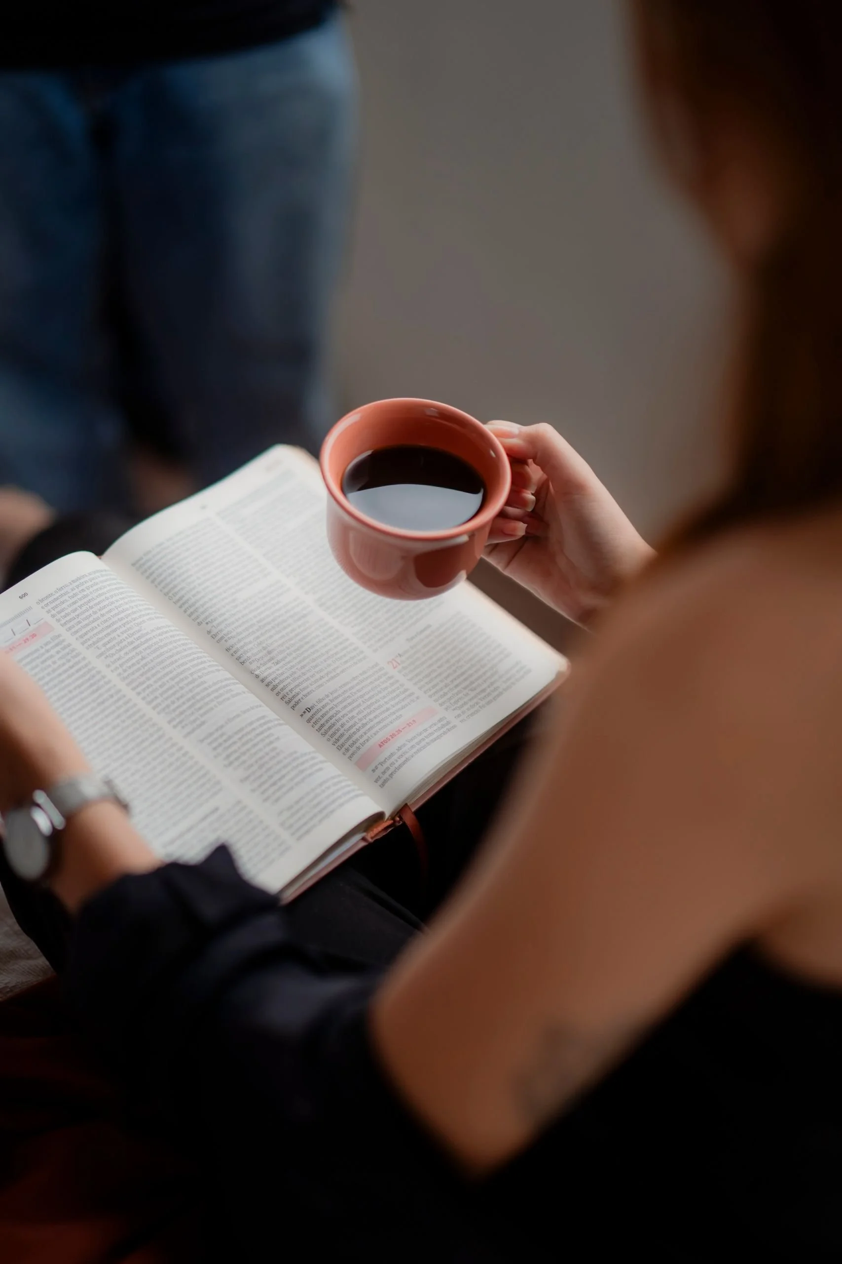 Person holding a cup of black coffee, reading a newspaper or magazine.