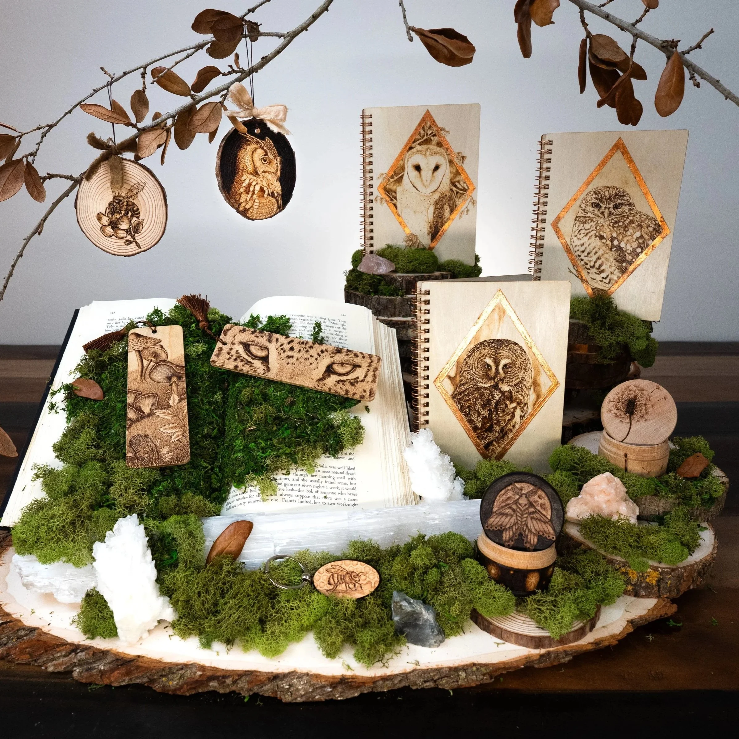 Display of woodland-themed artwork with engraved wood ornaments of animals, set among moss, leaves, and natural elements on a wooden base.
