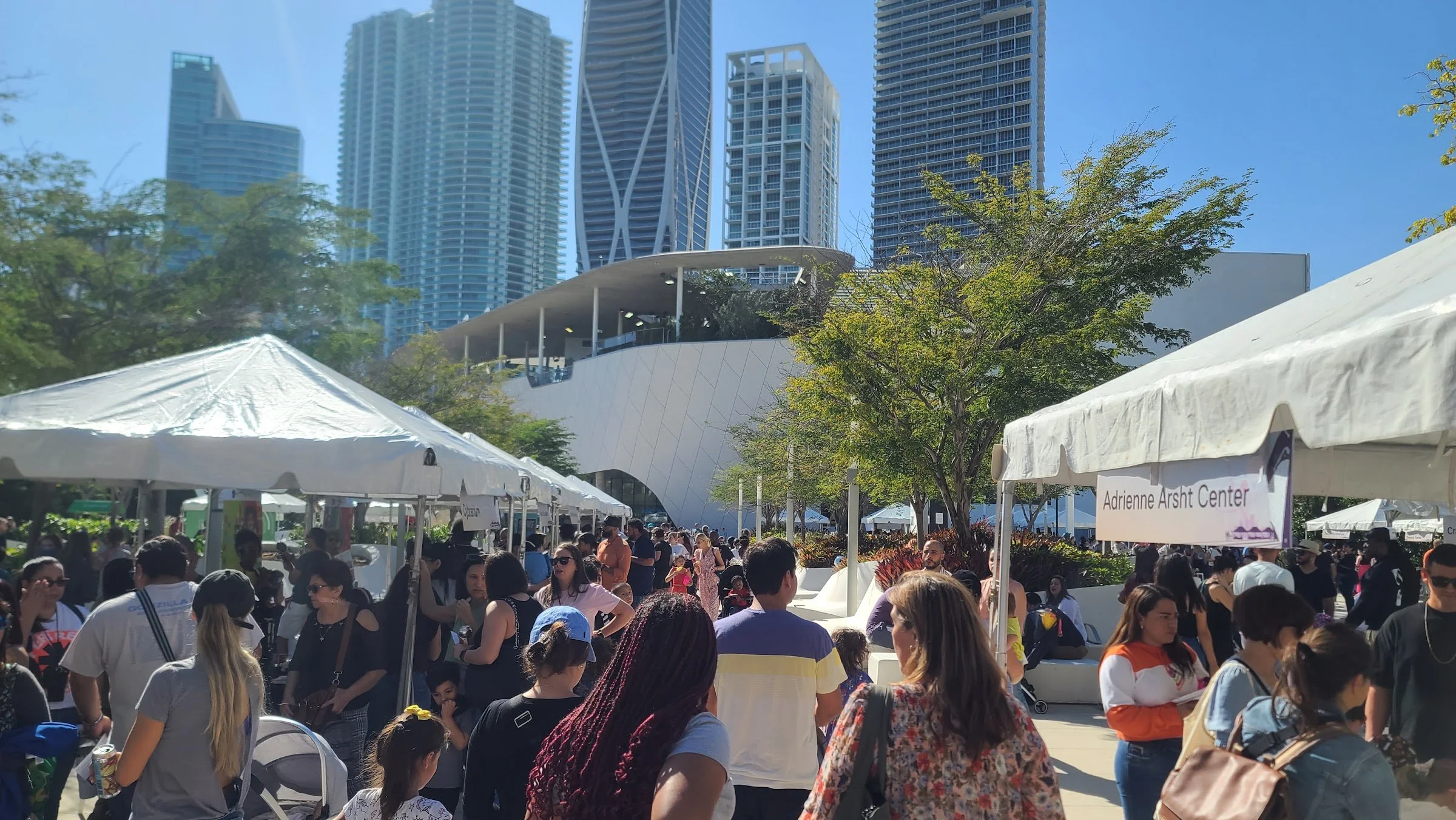Crowds at an outdoor community market under white tents in downtown Miami