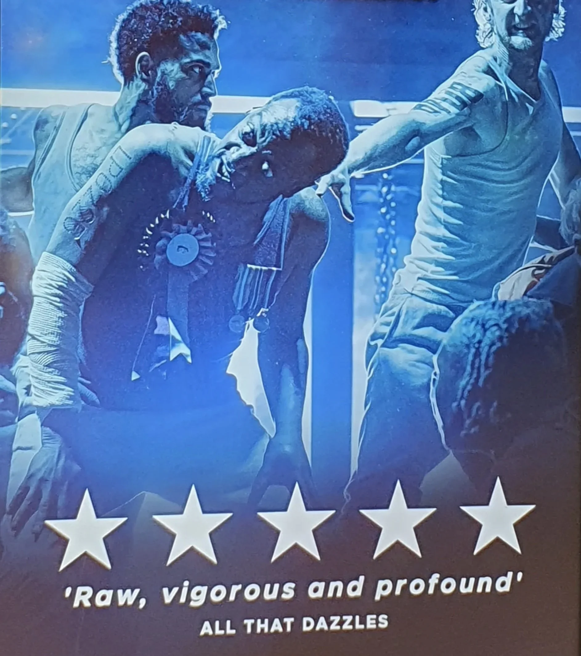 A poster with three men, one holding a microphone with a necklace with a large pendant, all wearing casual clothing. The poster features white star cutouts at the bottom and some unreadable text.