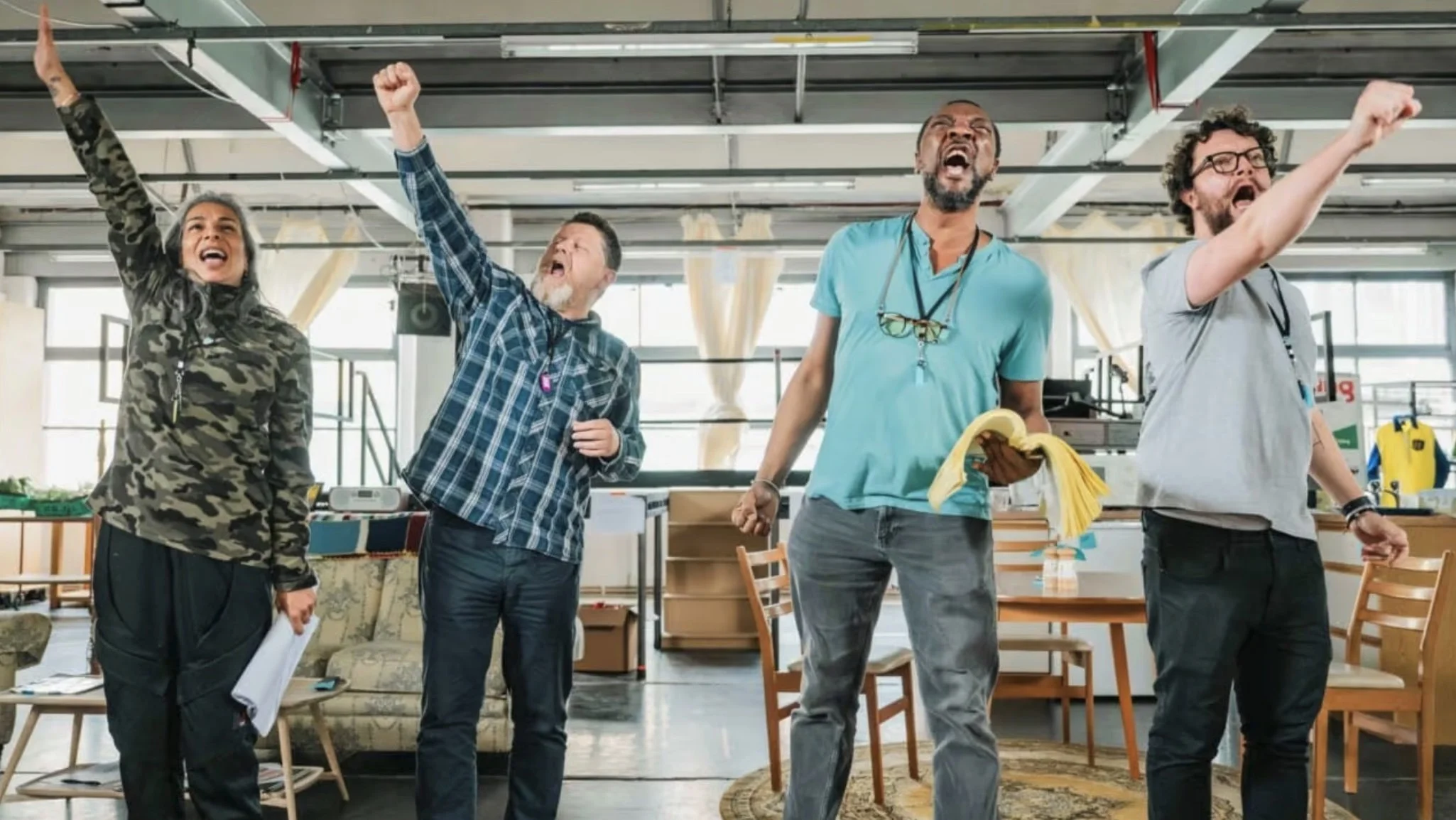Four people in an indoor space cheer and celebrate, raising their fists and shouting with enthusiasm.