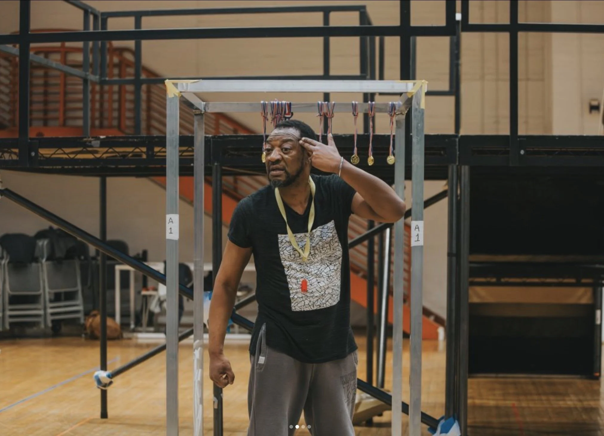 Man adjusting earphones on his head in an indoor gymnasium, with medals hanging on a structure behind him.
