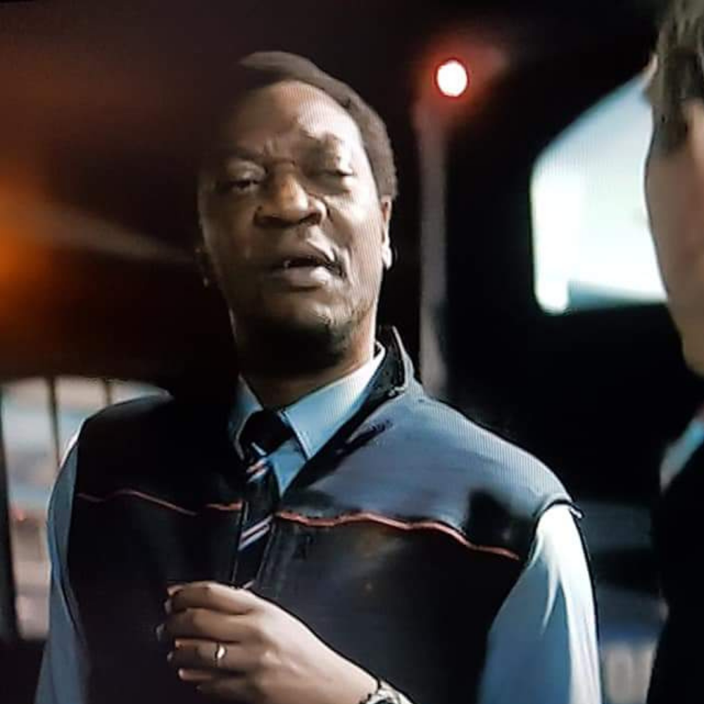 A man in a uniform with a tie, inside a vehicle, talking to someone outside the vehicle at night.
