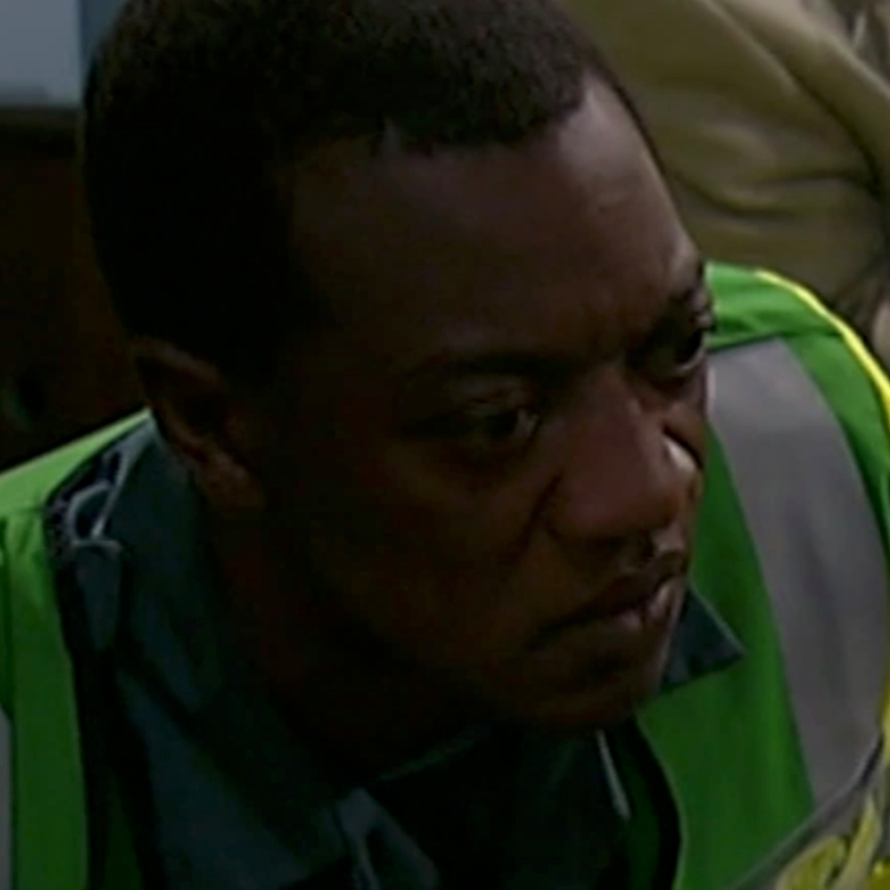 Close-up of a man with short dark hair wearing a green vest over a gray shirt.