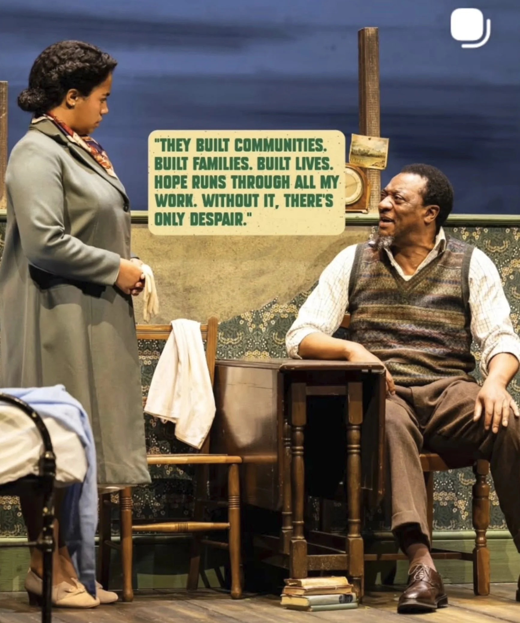A woman in a gray coat shaking hands with an older man sitting in a vintage armchair. The man is wearing a sweater vest and brown pants. There are books and a bag on the floor. A quote on the wall says, 'They built communities. Built families. Built 