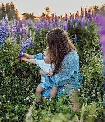 A woman with a child sitting in a flower garden, picking purple flowers.