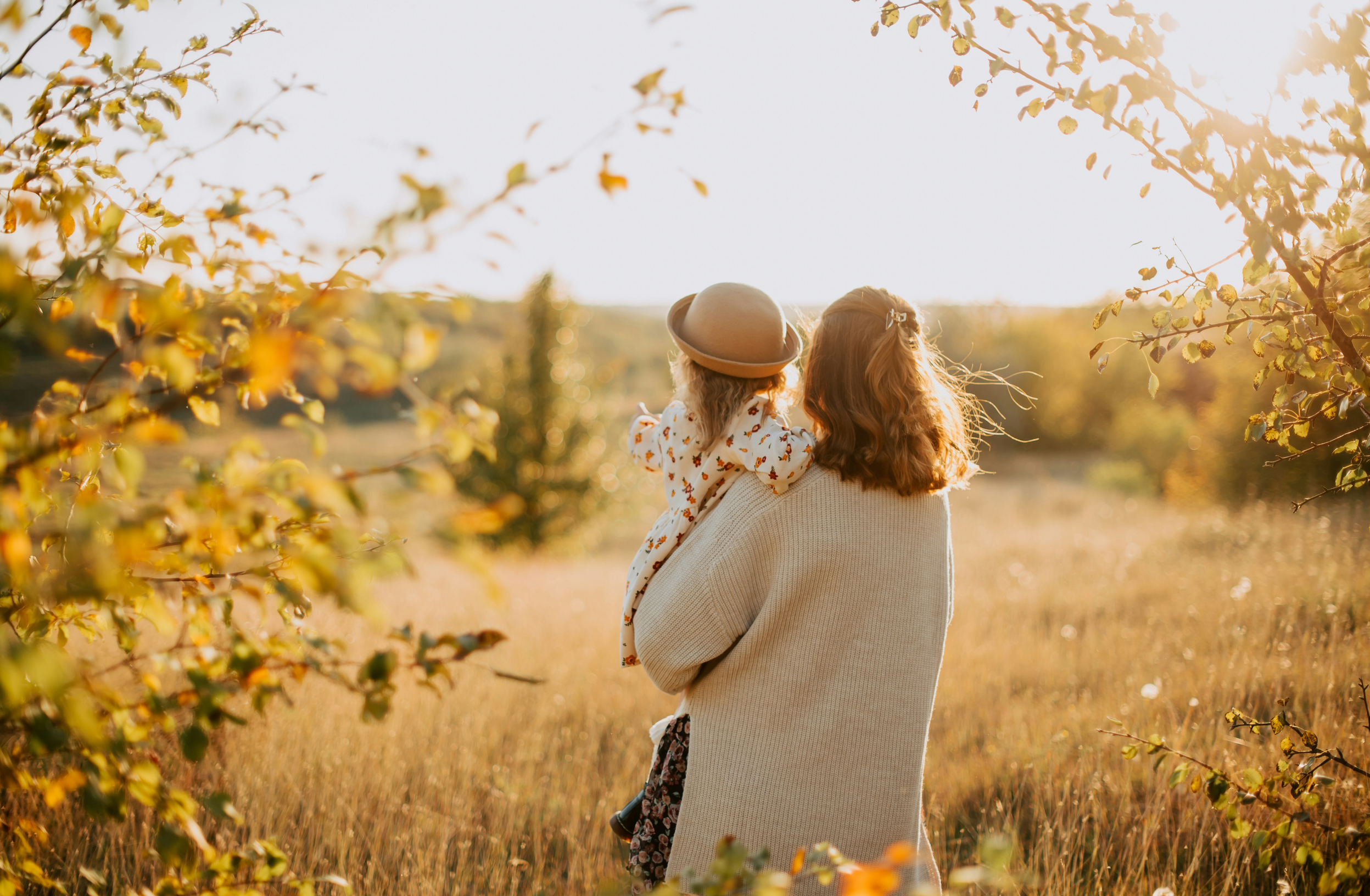 A woman carrying a child through a field filled with yellow flowers during sunset.