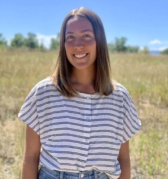 Anna Palombi, smiling outdoors in a sunny field, wearing a striped shirt.