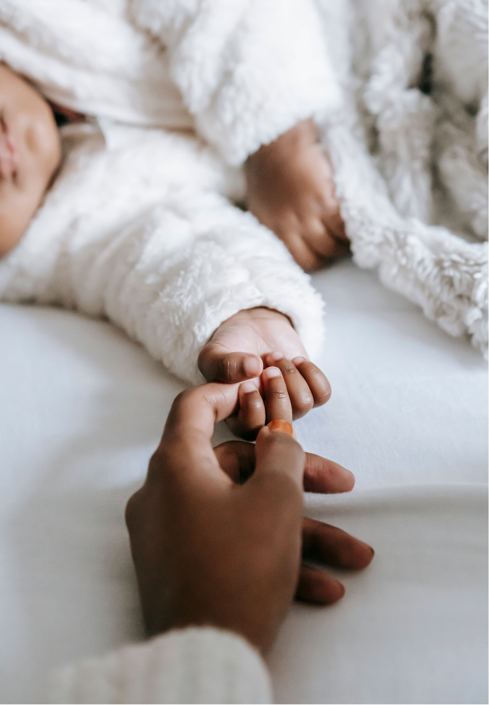 Close-up of a child's hand being gently held by an adult's hand on a soft white surface.