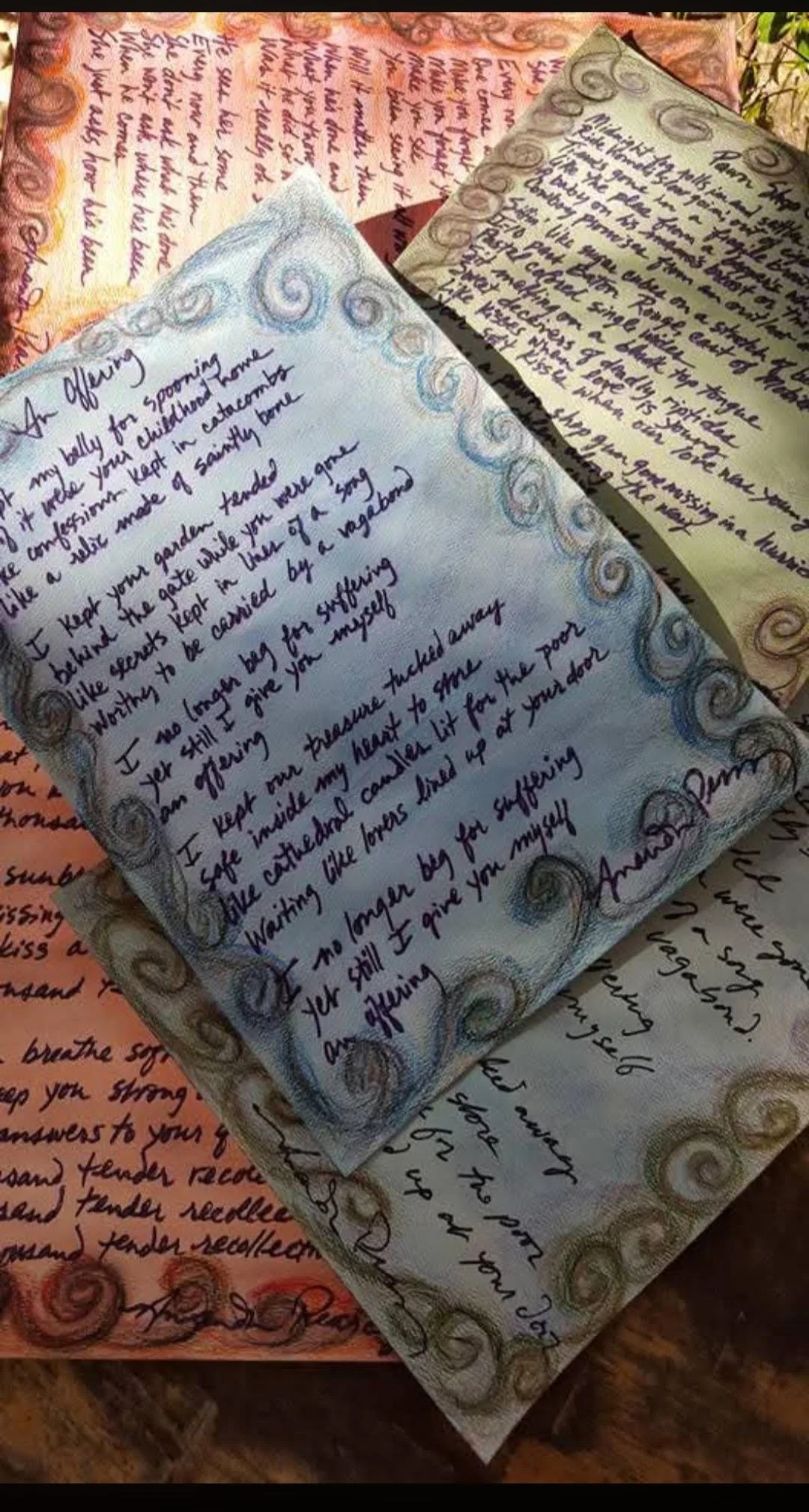Close-up of handwritten notes on decorative paper with a border of swirls and colorful accents, placed on other similar handwritten notes with decorative borders.