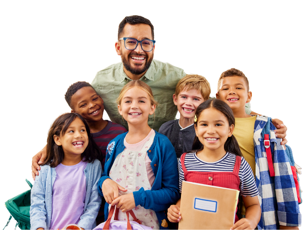 A smiling male teacher with glasses standing behind a group of diverse elementary school children, all smiling and holding books and school supplies.