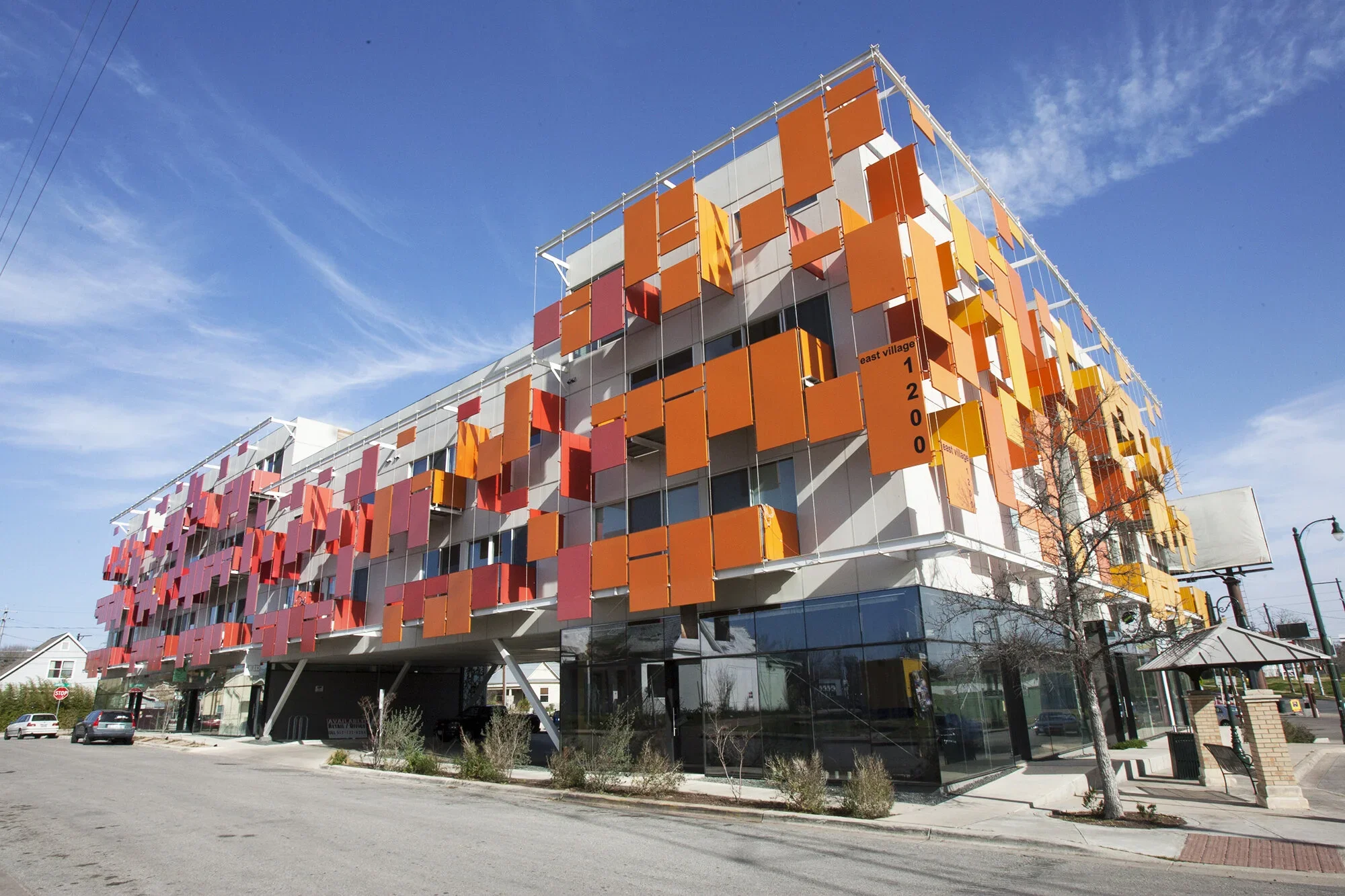 A modern multi-story building with colorful, orange and pink rectangular panels on its facade, set against a bright blue sky with some clouds.