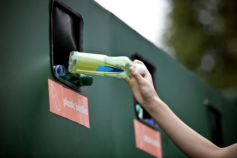 Person recycling plastic bottle in a recycling drop-off bin.