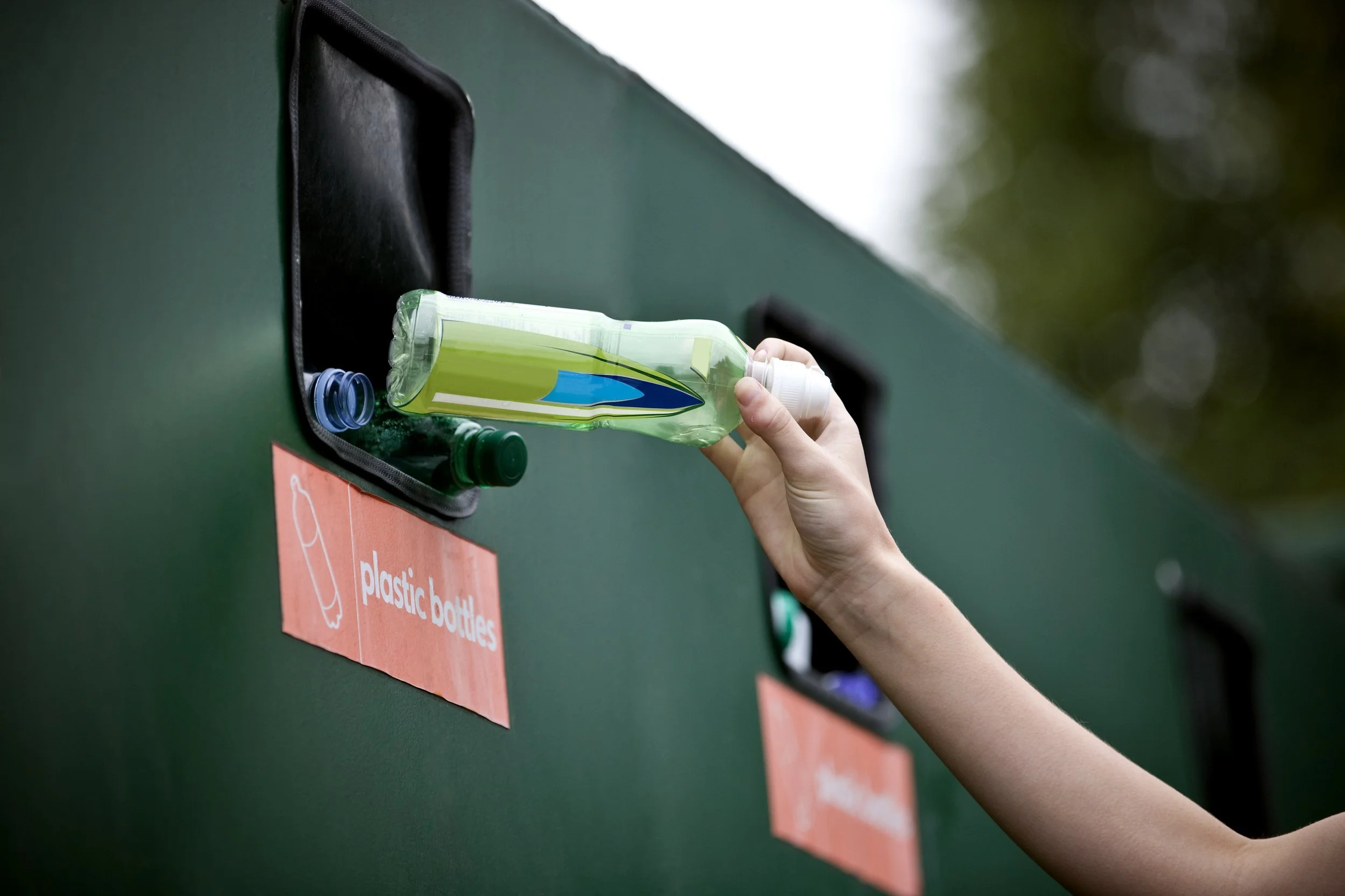Peron recycling plastic bottle in a recycling drop-off container.