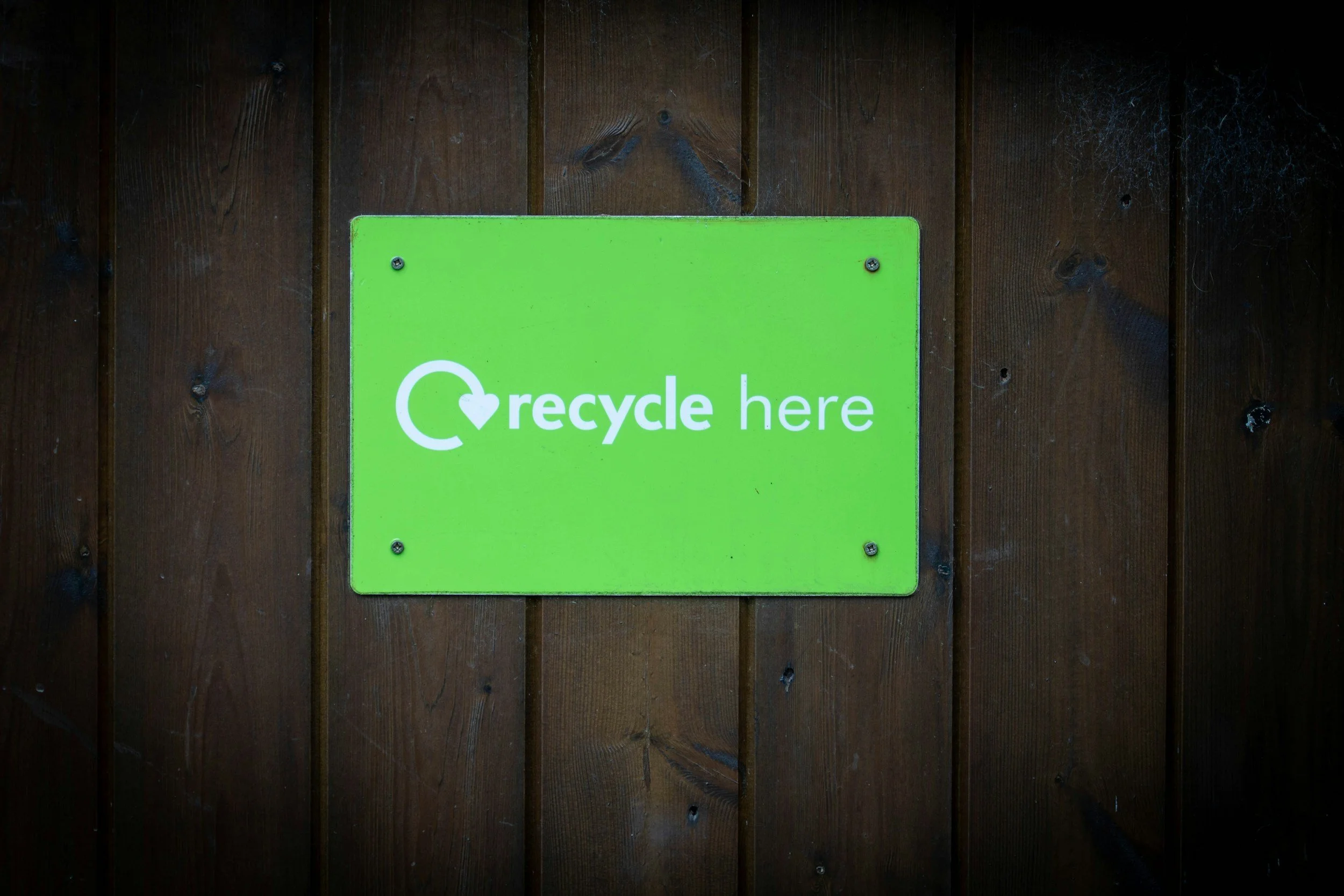 Sign stuck on fence. Sign says 'recycle here' with a circular arrow icon.