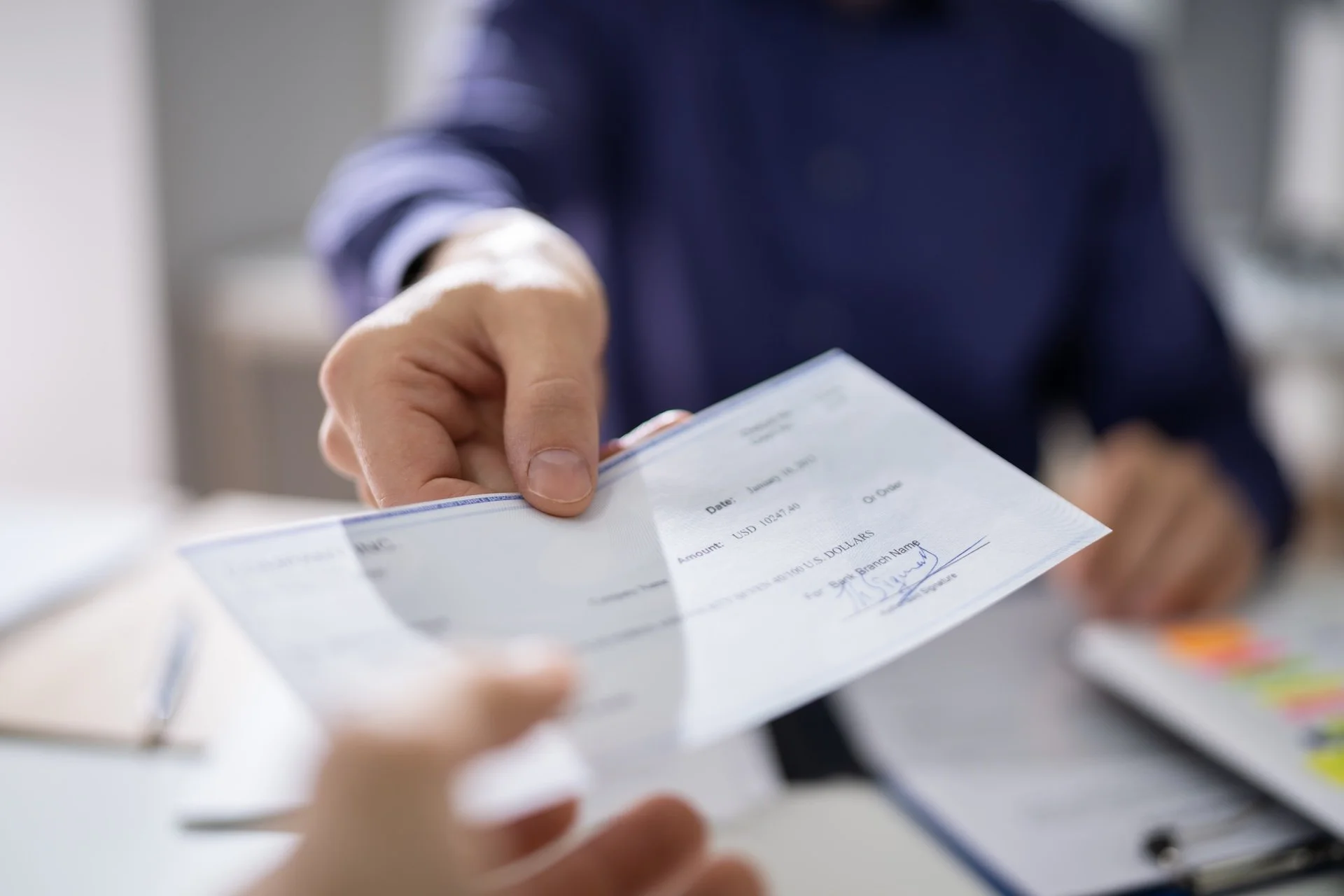 Close up of someone handing someone else a check. 