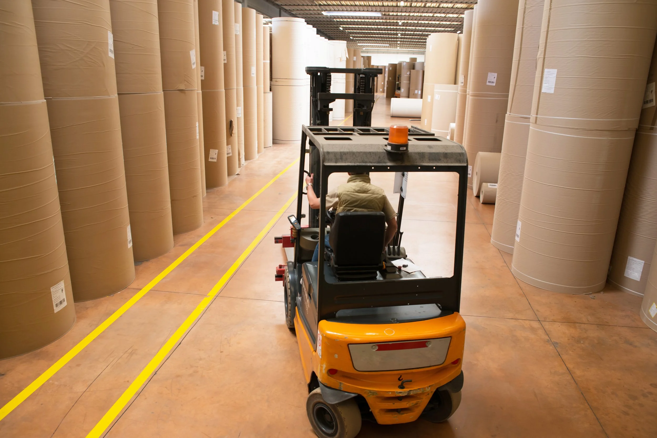 Forklift driving through large commercial roles of paper