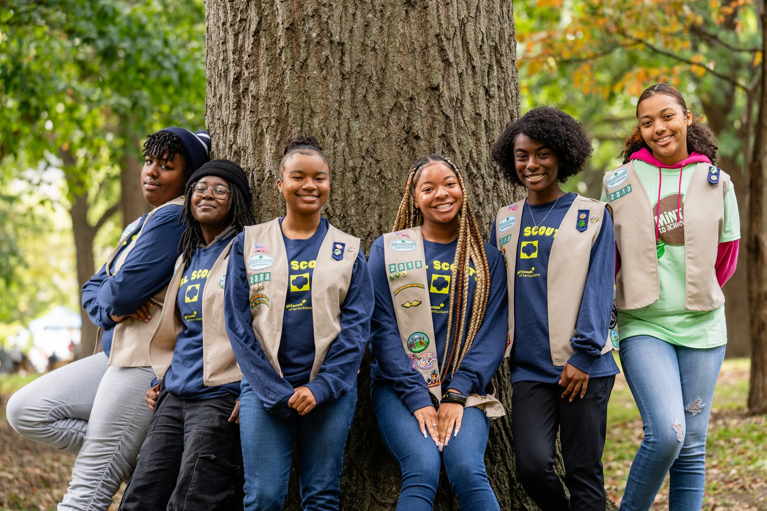 Girl Scouts standing together beside a large tree in a wooded park