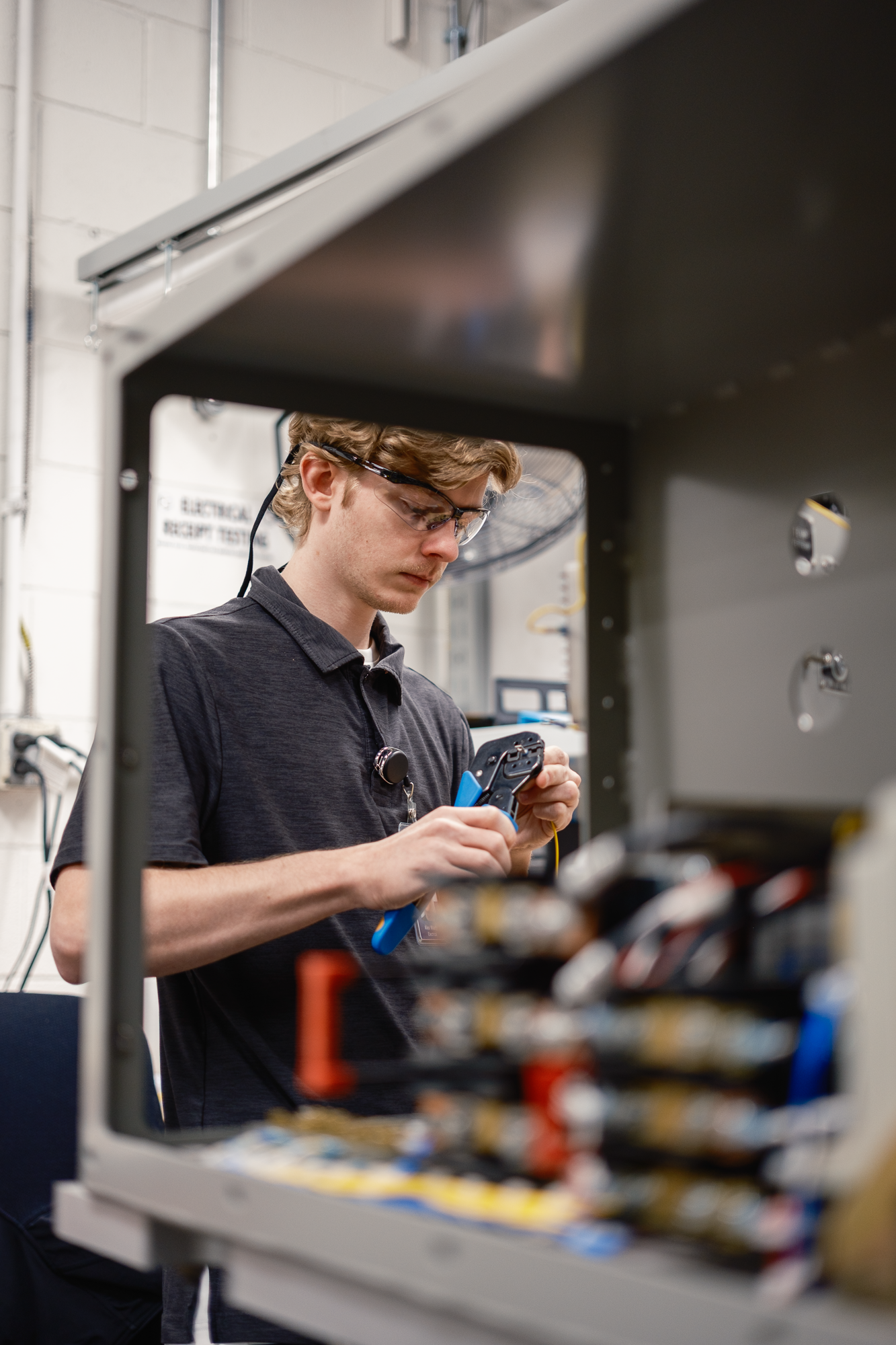 A young man with protective glasses working with electronic equipment in a lab or workshop environment.