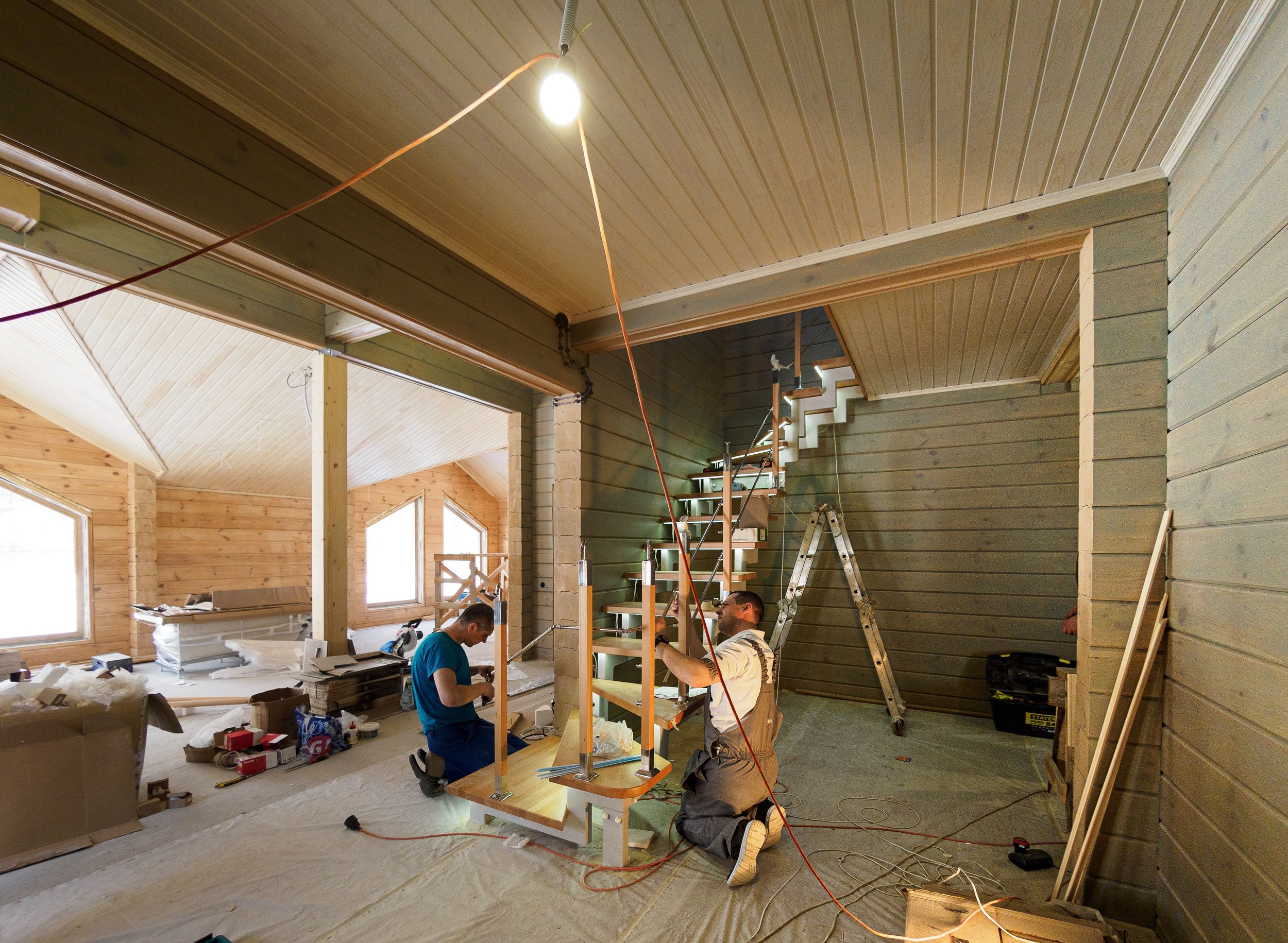 Interior of a house under construction with workers installing stairs and working on the walls and ceiling.