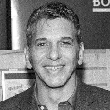 A smiling man with short hair in formal attire in front of a background with text.