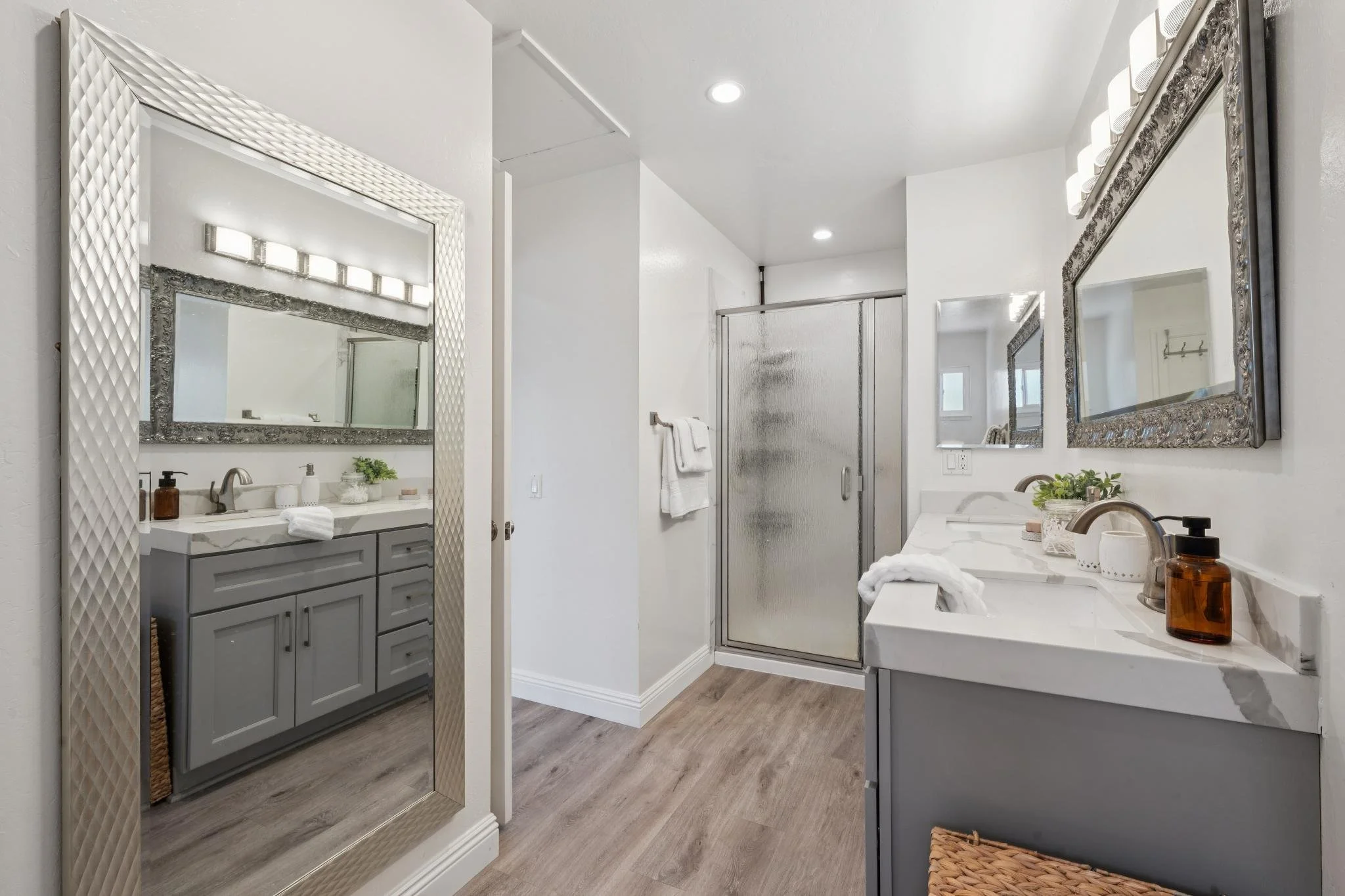 A modern bathroom with a large mirror, a double sink vanity, a glass shower enclosure, and white and gray decor.