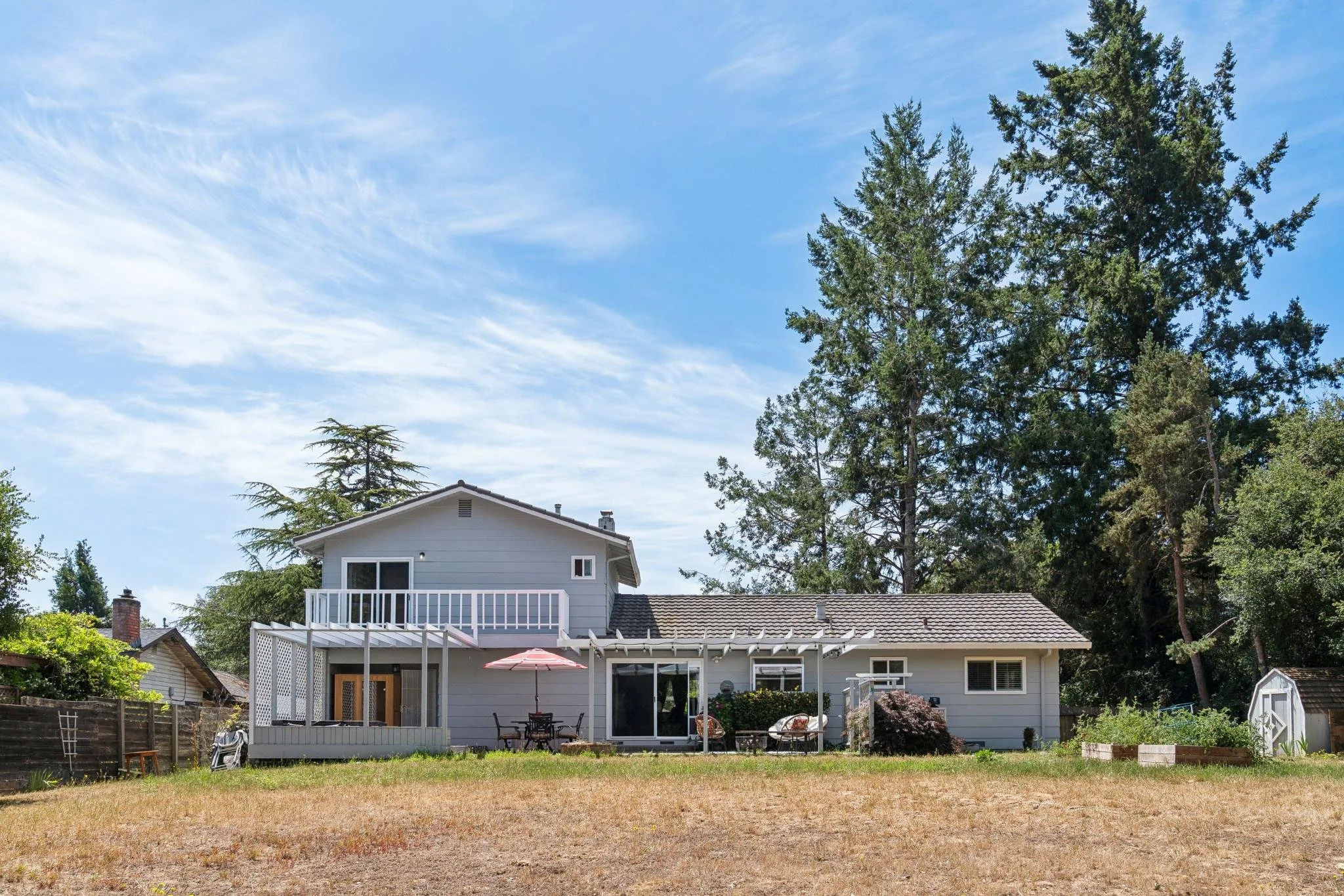 A two-story white house with a balcony, a patio with outdoor furniture, and a backyard with trees and a lawn.