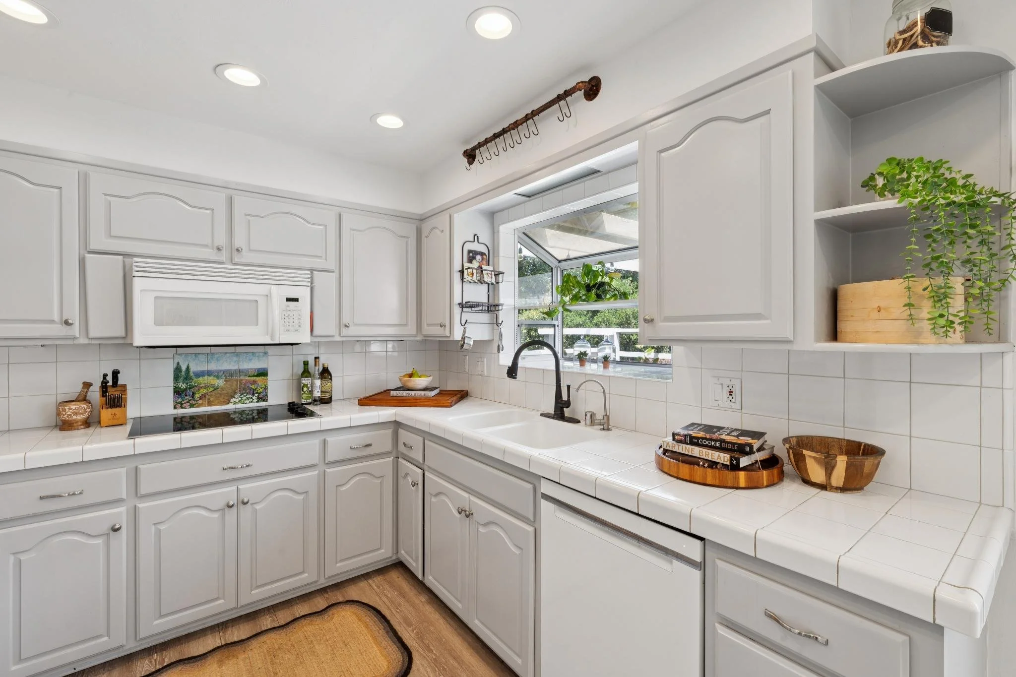 White kitchen with cabinets, a microwave, potted plants by a window, and kitchen countertops.