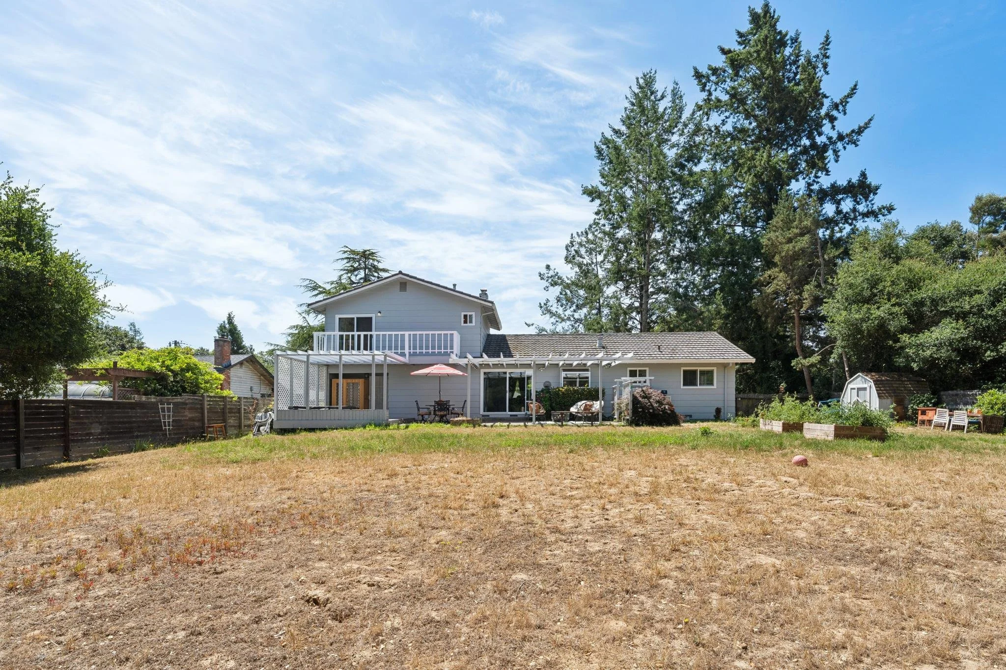 Backyard with a house, outdoor furniture, trees, and a partly cloudy sky.