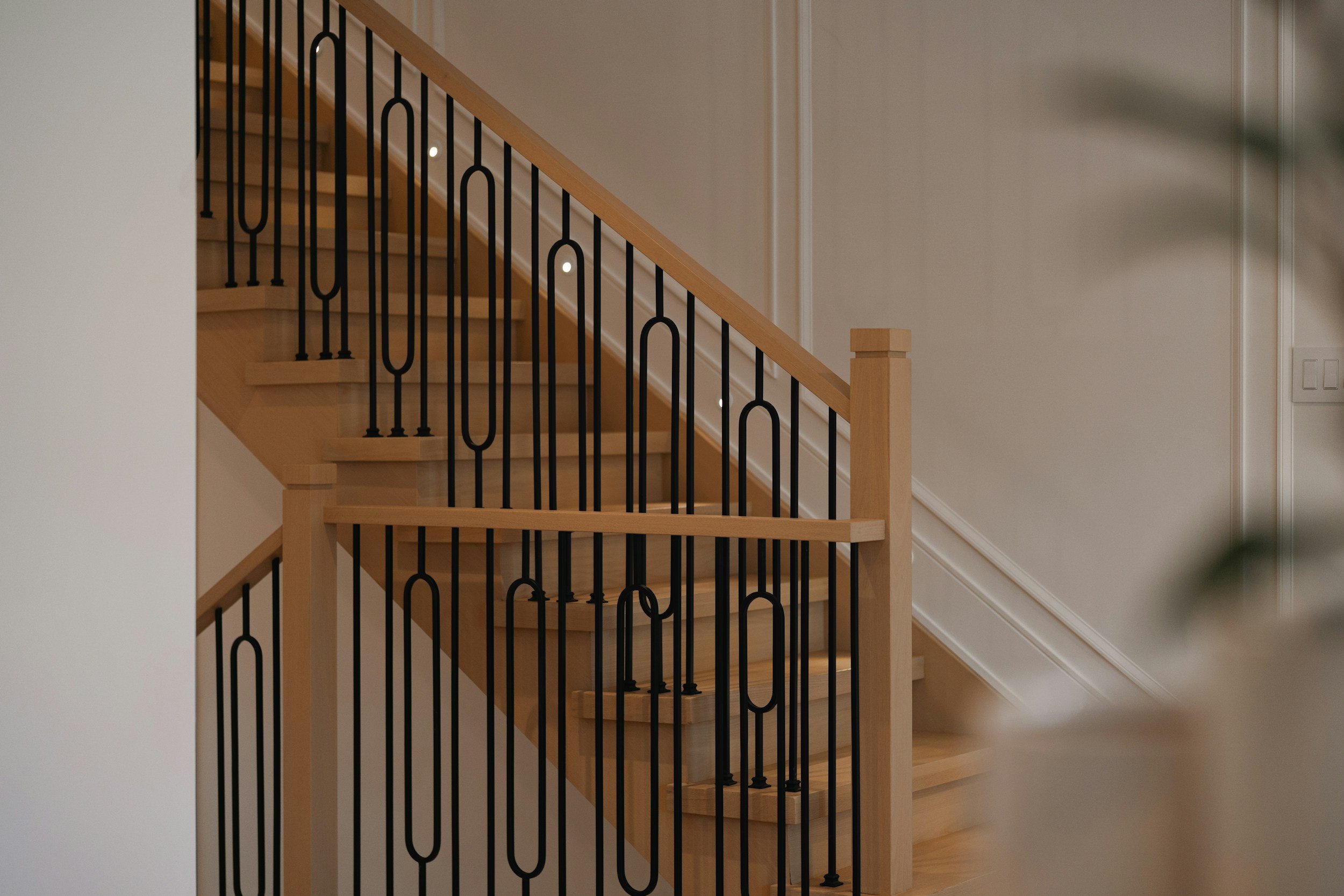 Wooden staircase with black metal balustrade, inside a house with beige walls and white trim.