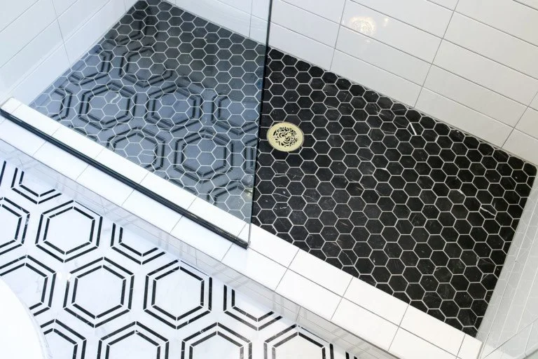 A shower with a glass door, black hexagonal tiles on the shower floor, and white tiles on the bathroom floor featuring a hexagon pattern.