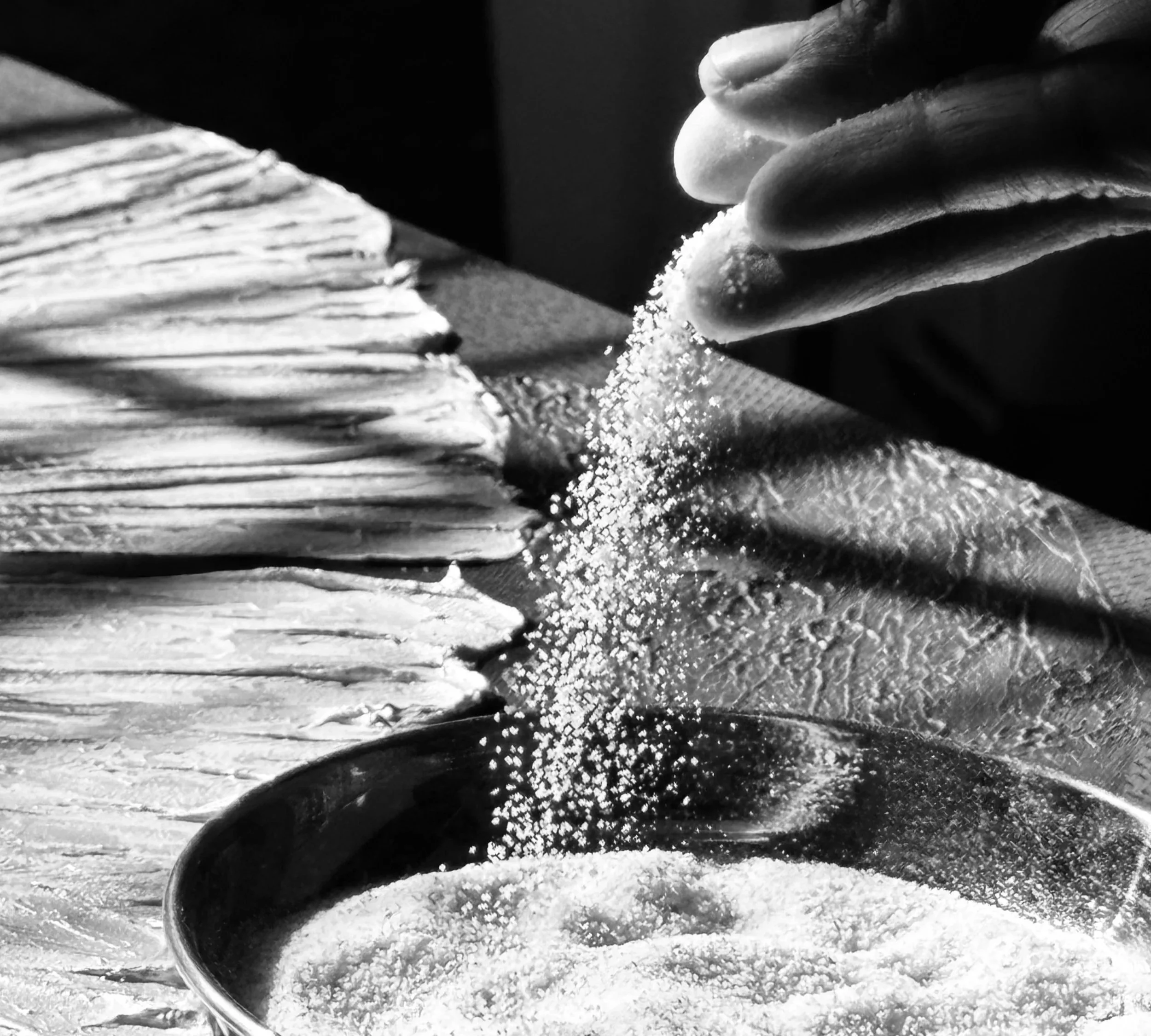Close-up of a person's hand gripping a kitchen knife as they chop or grind a substance on a textured surface, with small particles falling from the substance.