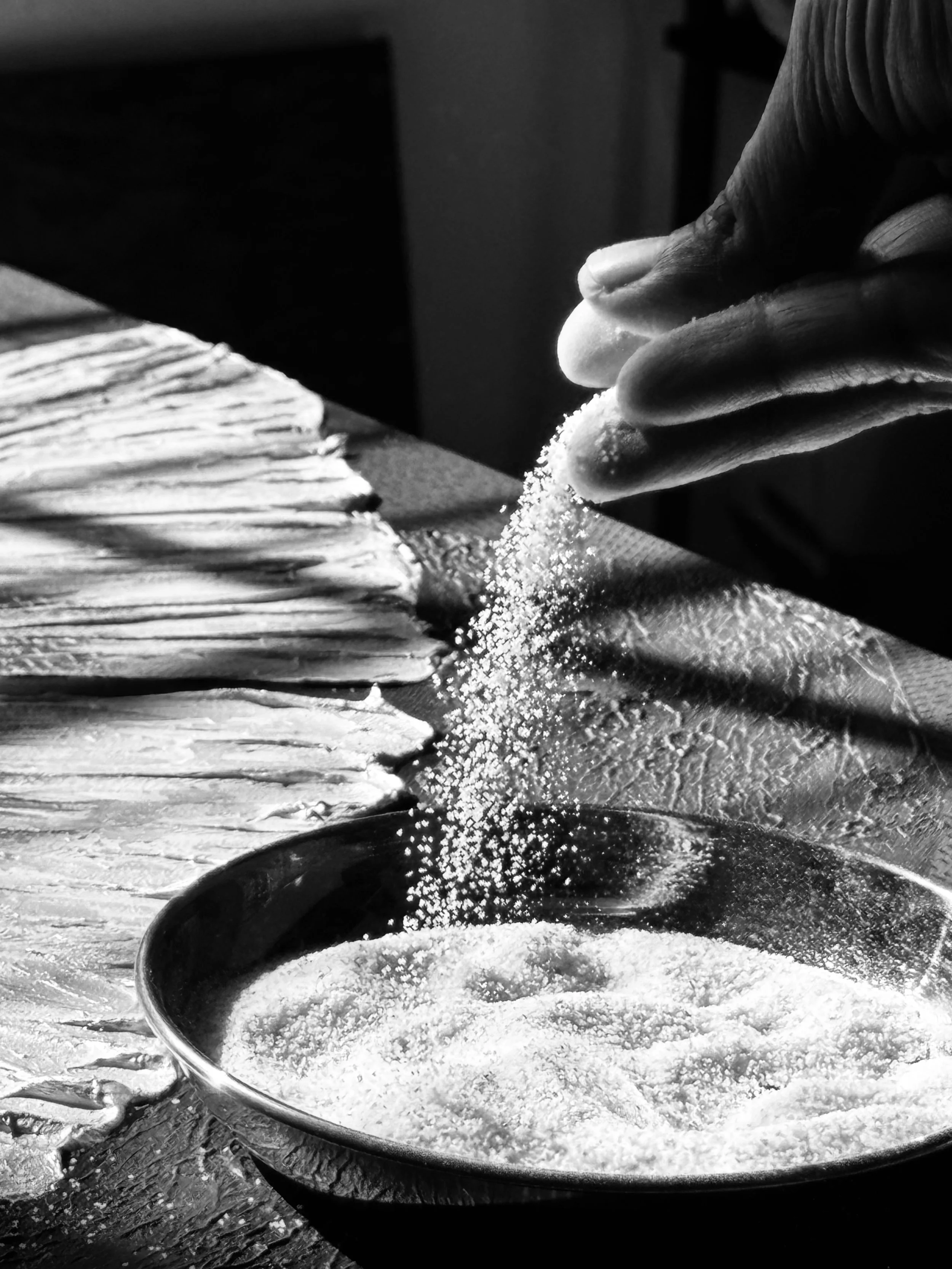 A hand sprinkling a white grainy substance into a large black bowl filled with the same substance.