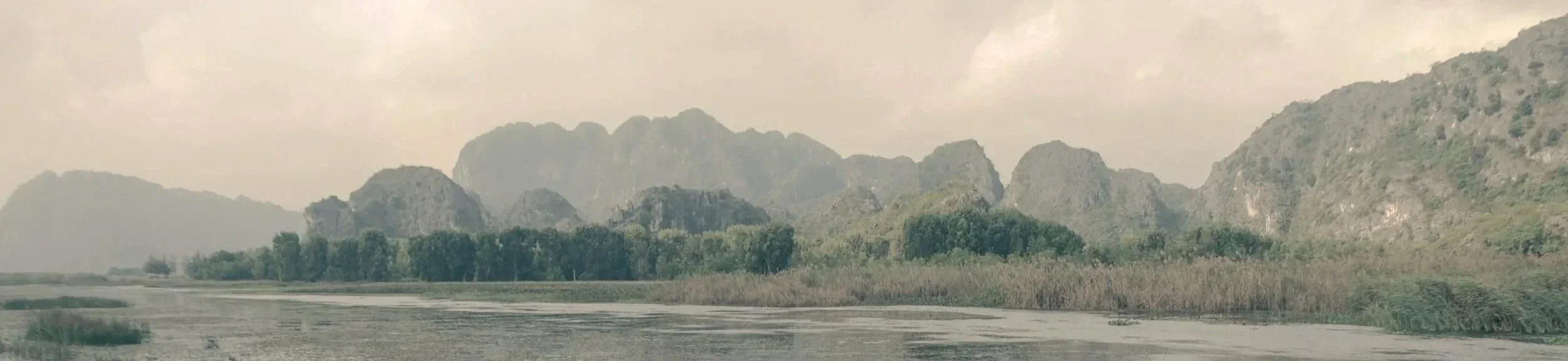 Landscape of tall mountains with forested bases and a river in the foreground.