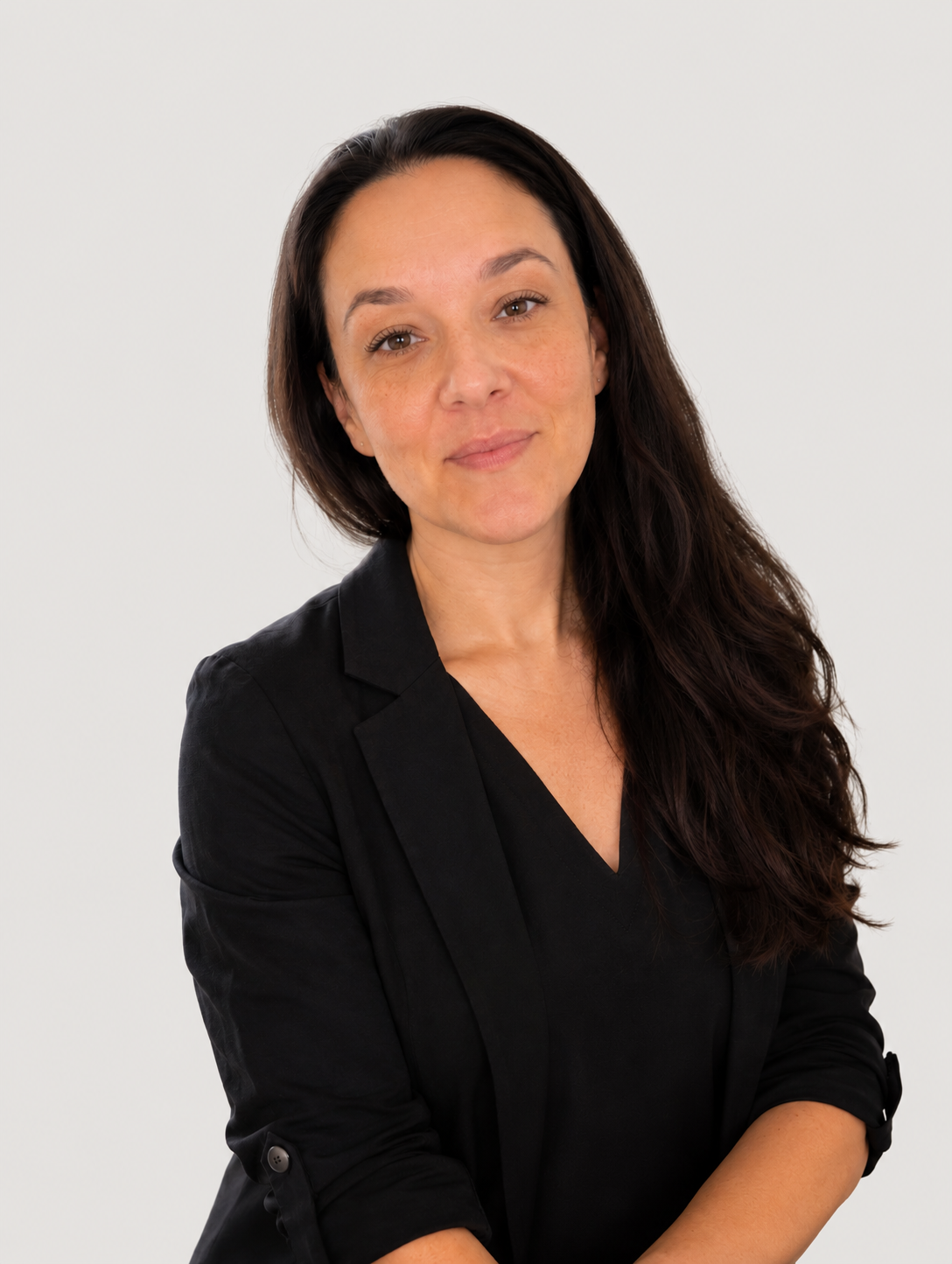 A woman with long dark hair, wearing a black blazer, looking at the camera with a slight smile, standing against a plain white background.