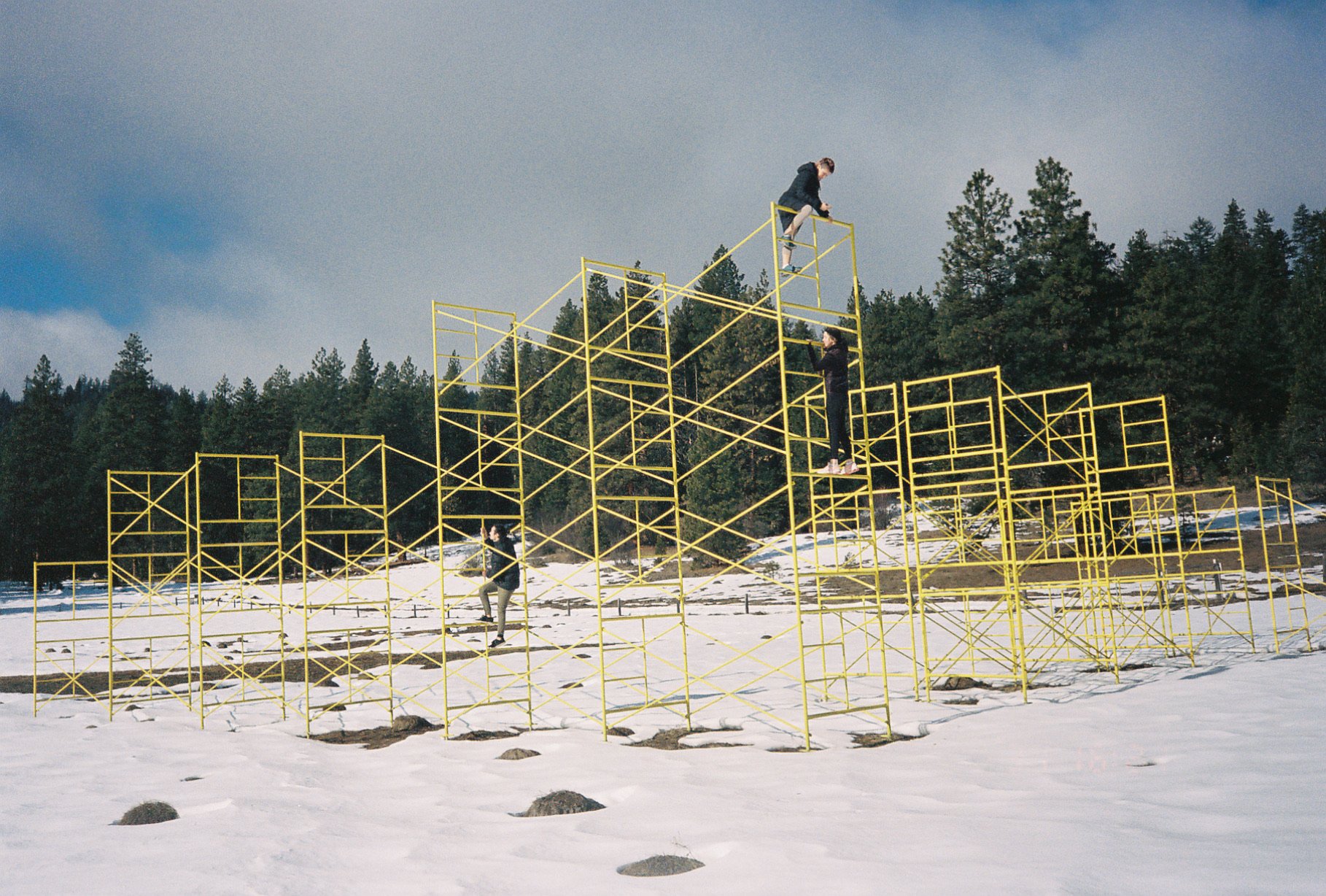 People climbing a large yellow geometric sculpture in a snowy landscape near Ashland, Oregon, photographed on 35mm film.