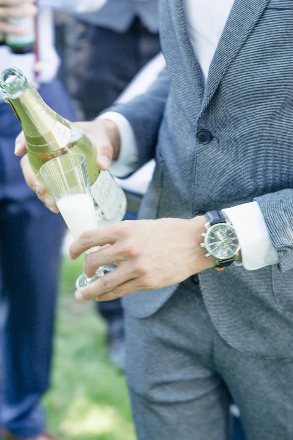 Ein Mann in einem grauen Anzug füllt ein Glas mit Sekt auf einer Feier.