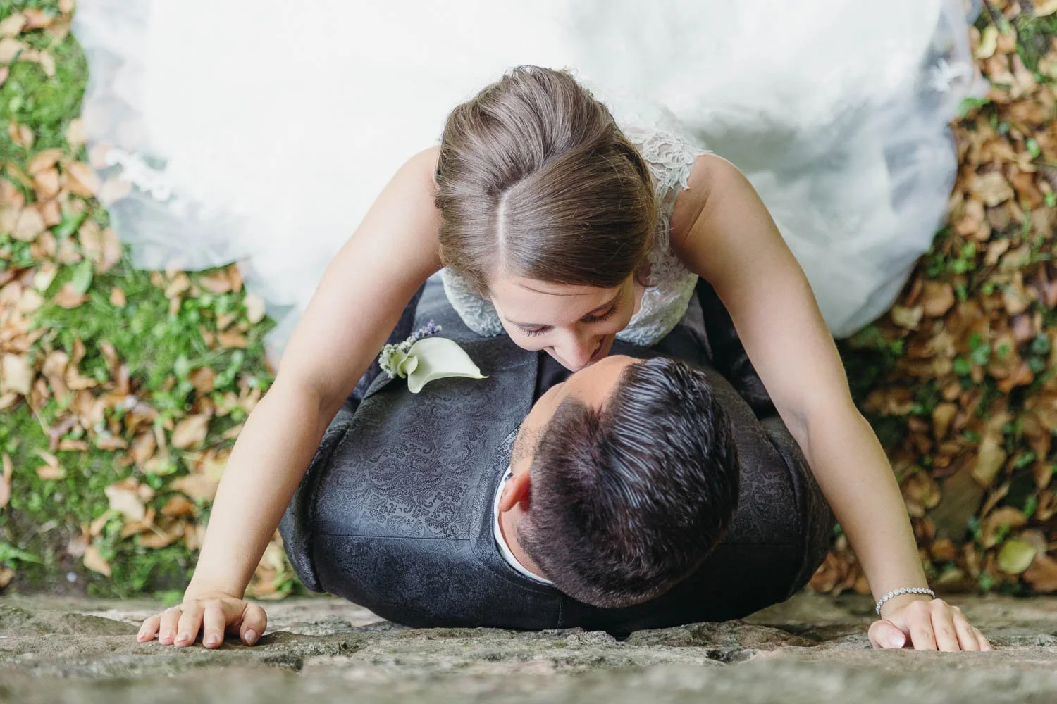 Ein Brautpaar, das sich bei ihrer Hochzeit küsst, von oben fotografiert, auf einem steinigen Boden mit Herbstlaub im Hintergrund.
