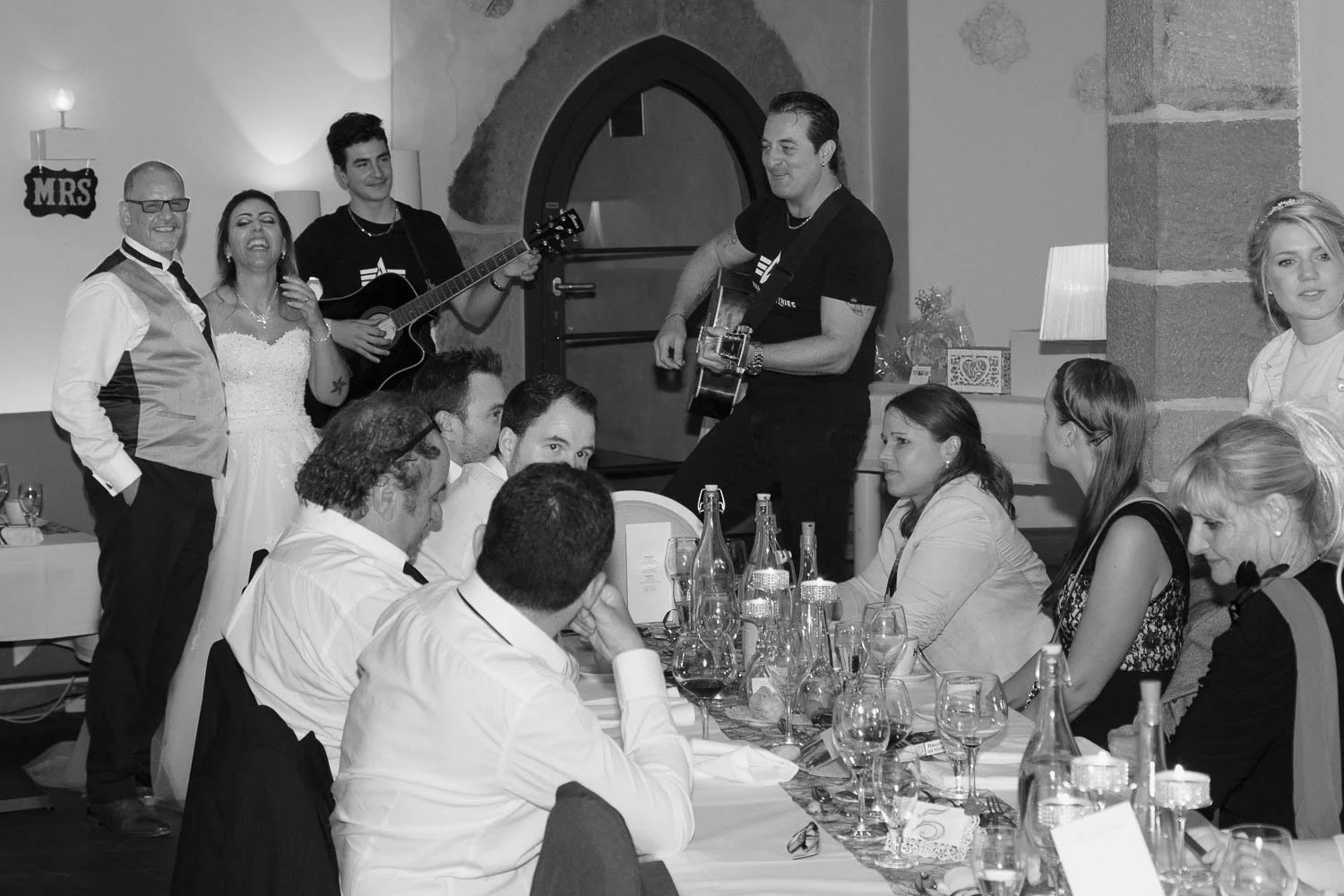 Menschen bei einer Feier, die Musik machen, während die Gäste am Tisch sitzen.