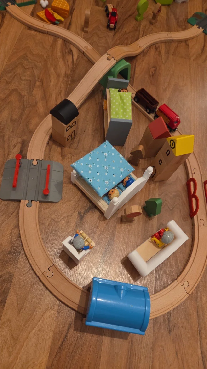 Spielzeugzug mit Schienen, kleinen Gebäuden, Figuren, und Fahrzeugen auf Holztisch.