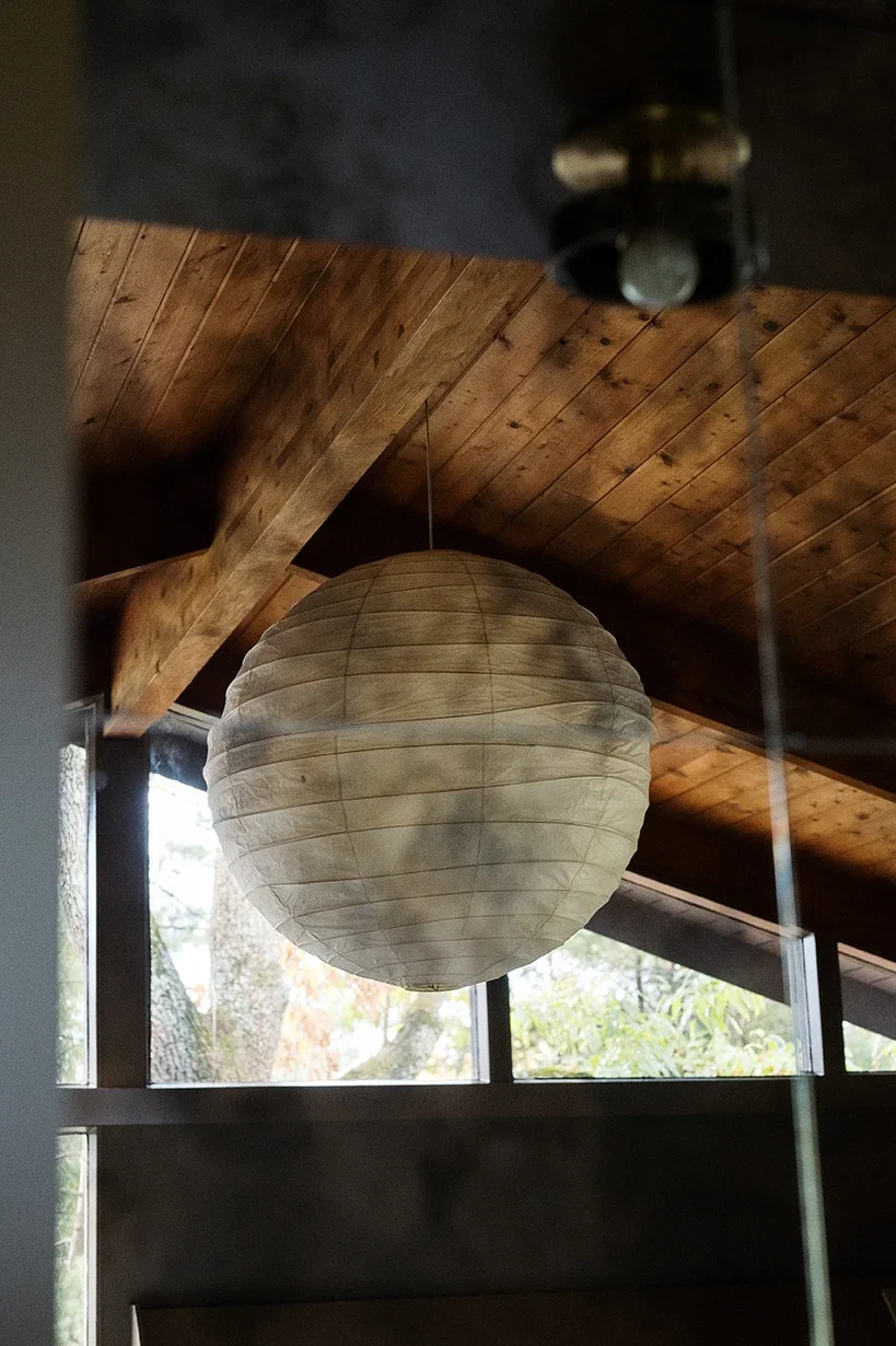 White paper lantern hanging from a wooden ceiling in a room with large windows.