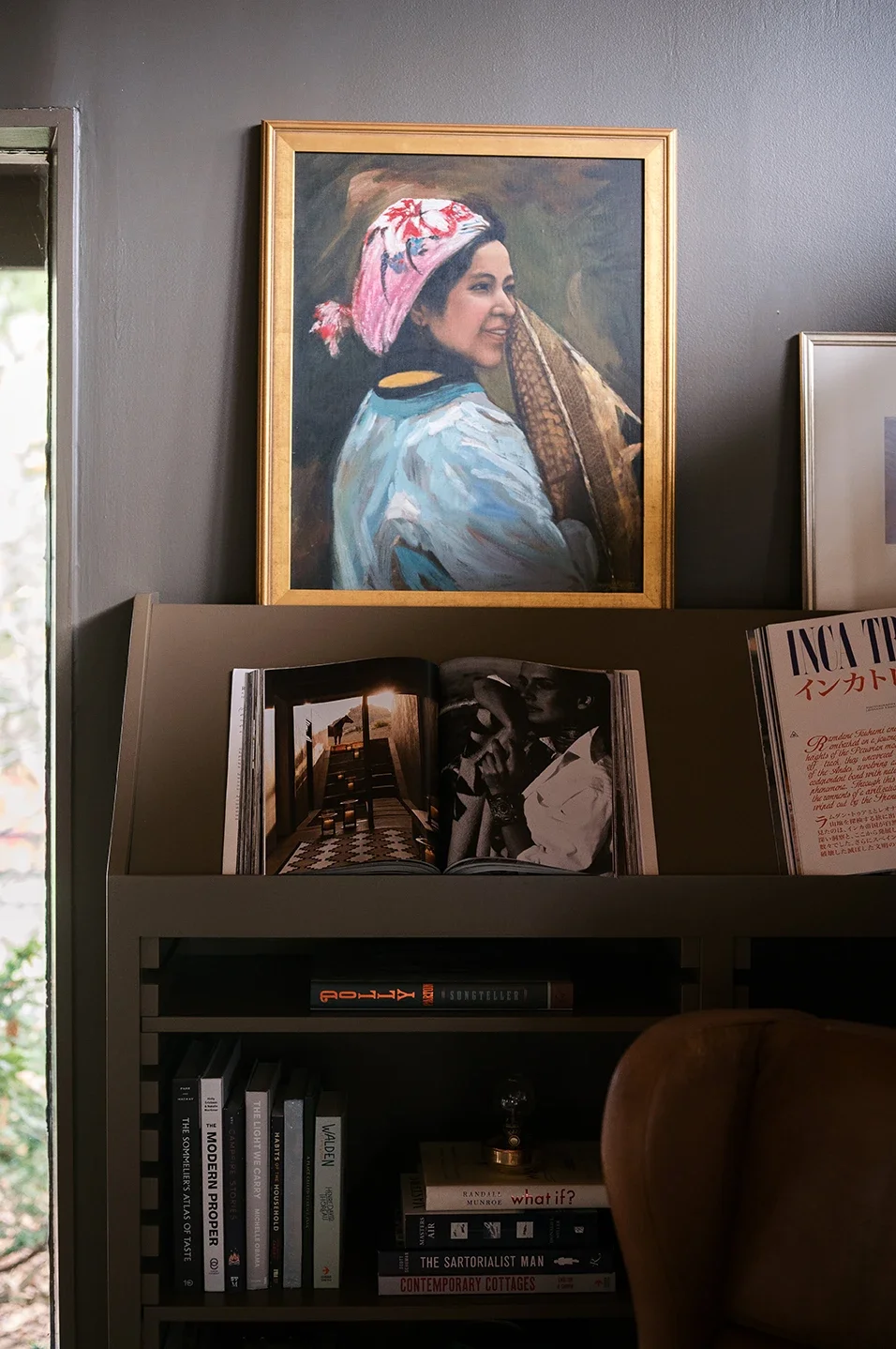 Portrait painting of a woman wearing a pink headscarf and a blue and white outfit, smiling and looking to the side, hanging on a wall.
