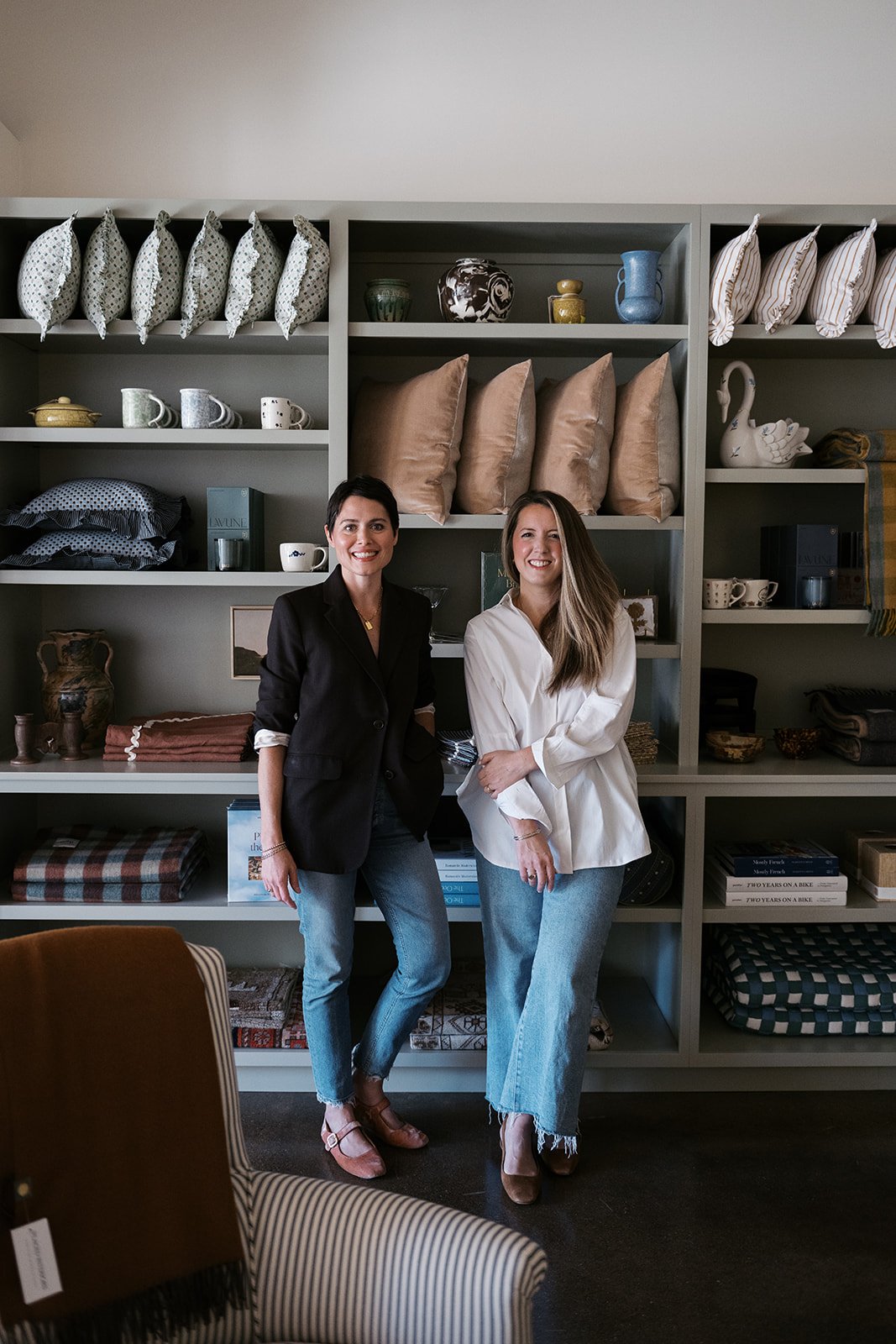 Two women standing in front of a well-stocked bookshelf, smiling at the camera.