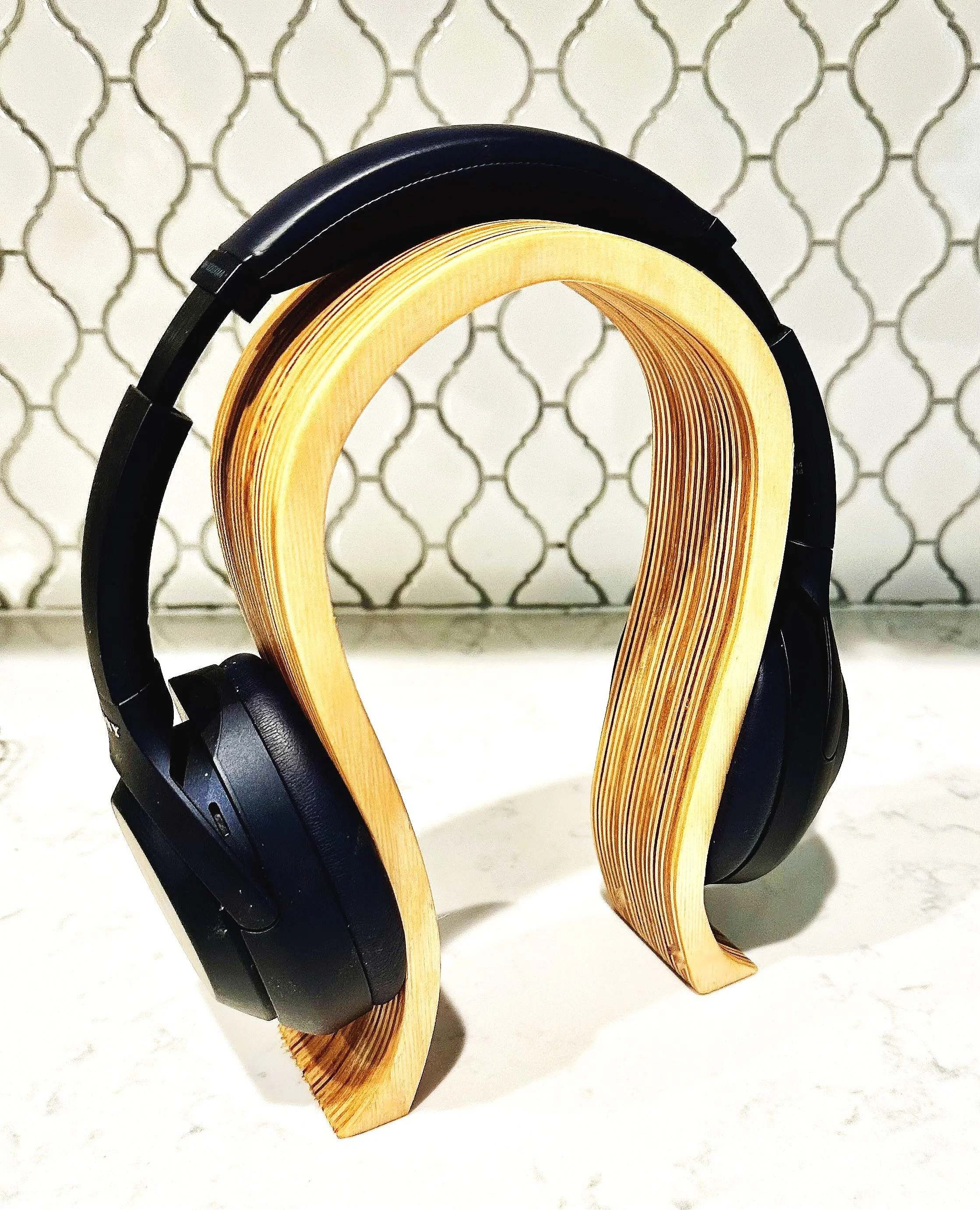 A pair of black headphones and two wooden headphone stands on a white surface with a patterned background.