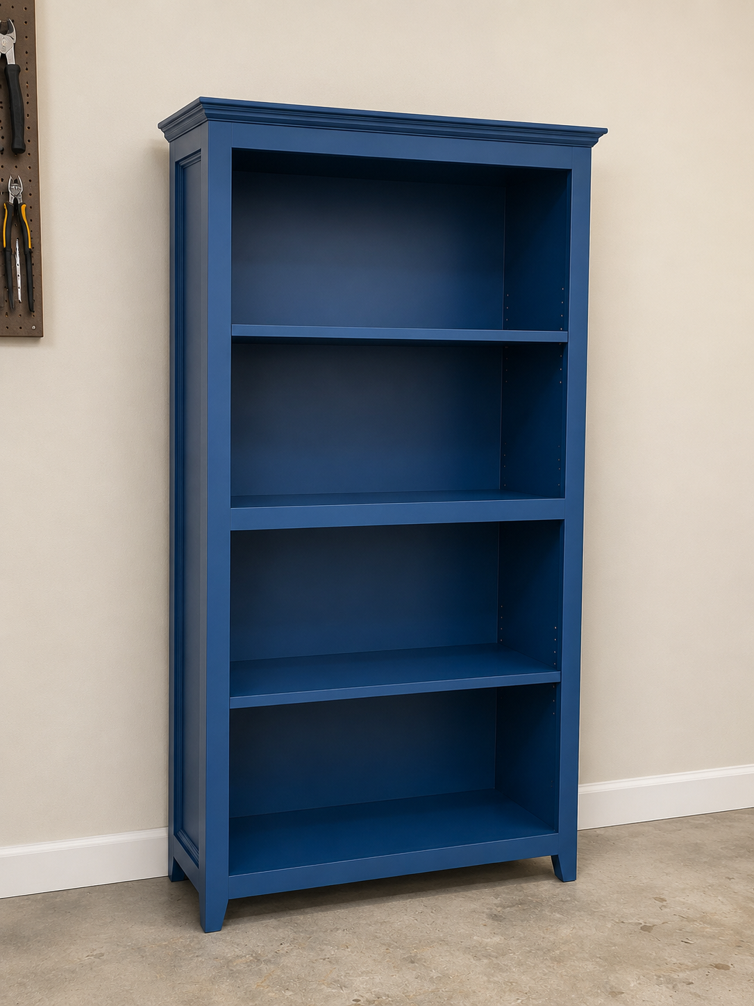 A tall blue bookshelf with four empty shelves standing against a white wall in a room with beige carpet.