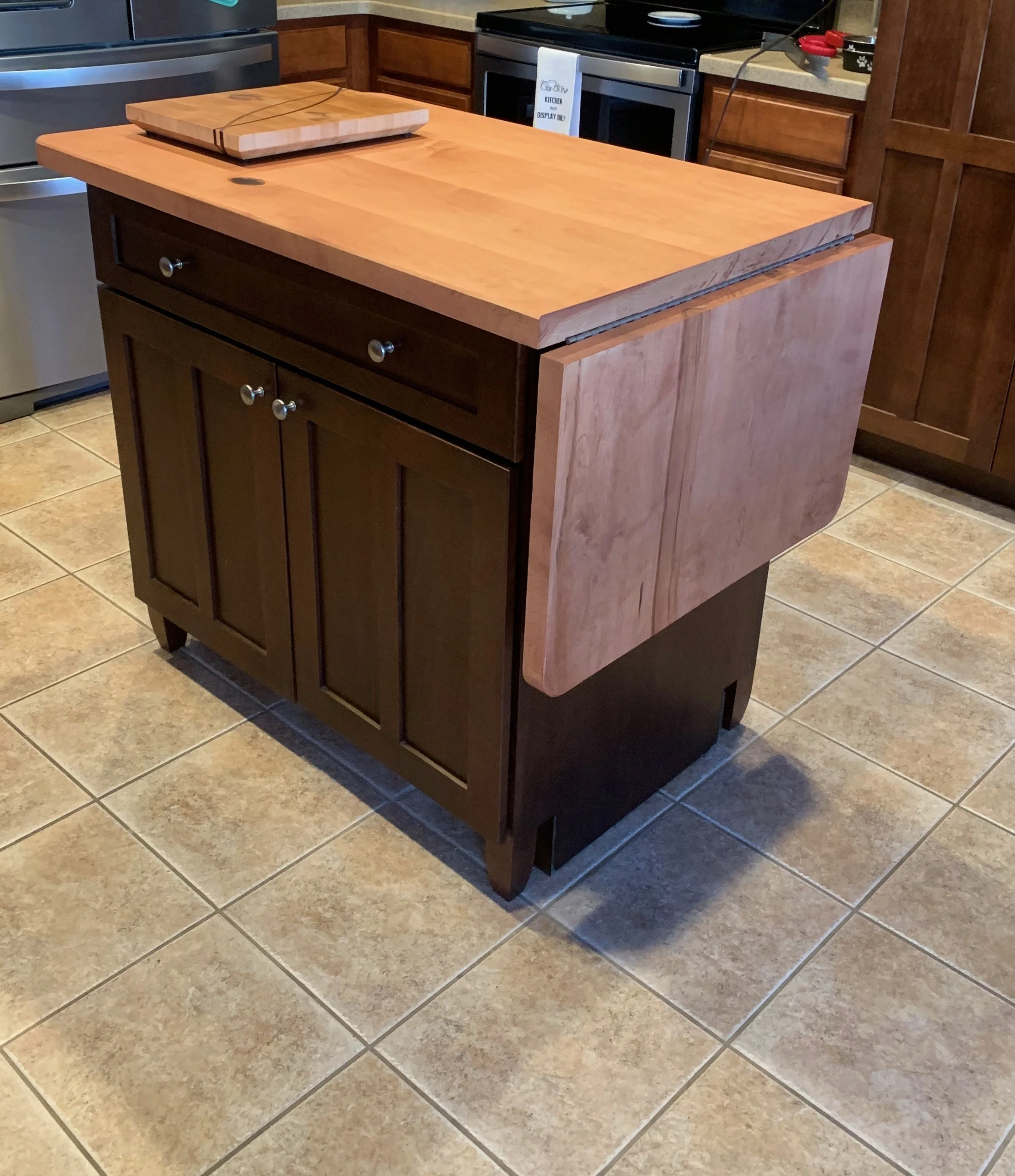 Kitchen with a wooden island, a cutting board on top, a stove, and wooden cabinets.