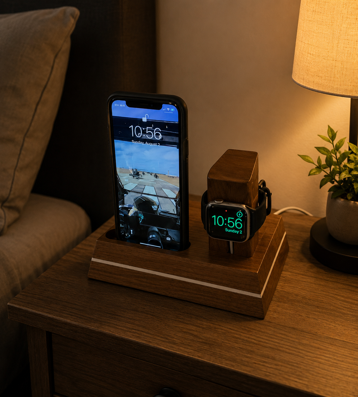 A wooden table with a smartphone and smartwatch on a wooden stand, a potted plant, and a beige lampshade in a cozy living room.